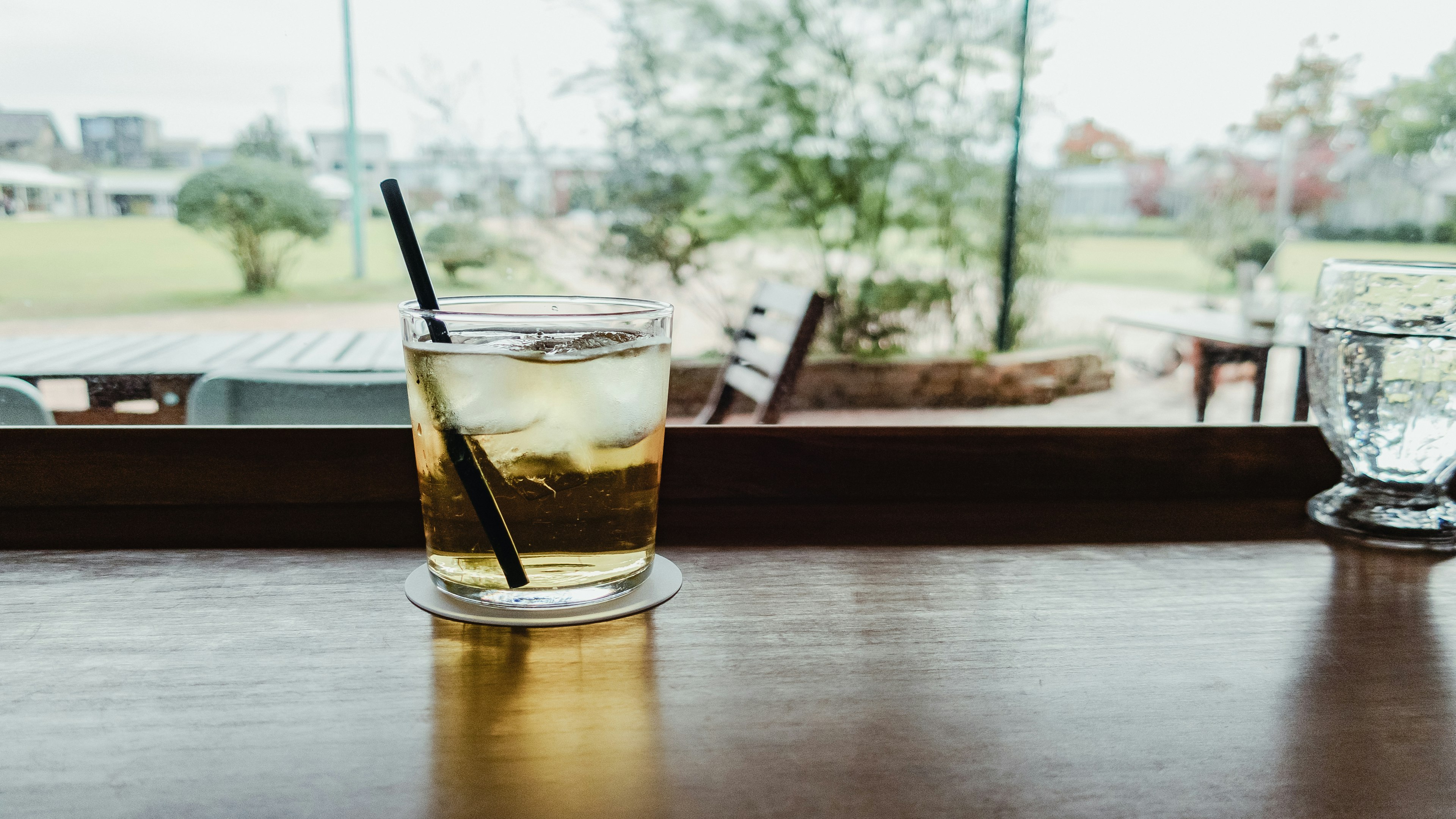 A glass of iced drink on a wooden table with a view of greenery outside