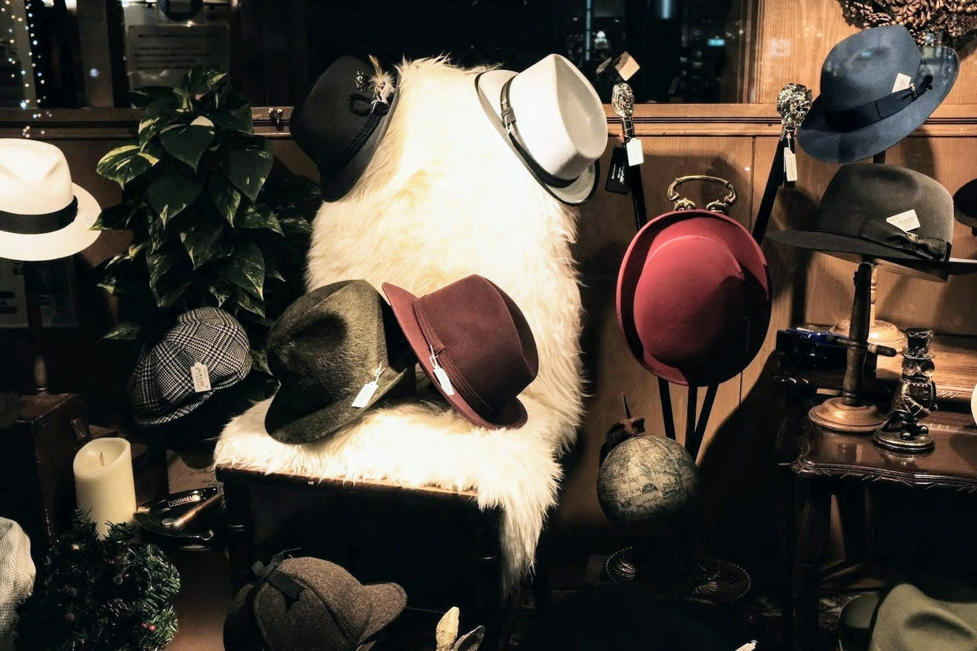 A collection of hats displayed on a chair with a faux fur throw and plants in a cozy shop setting