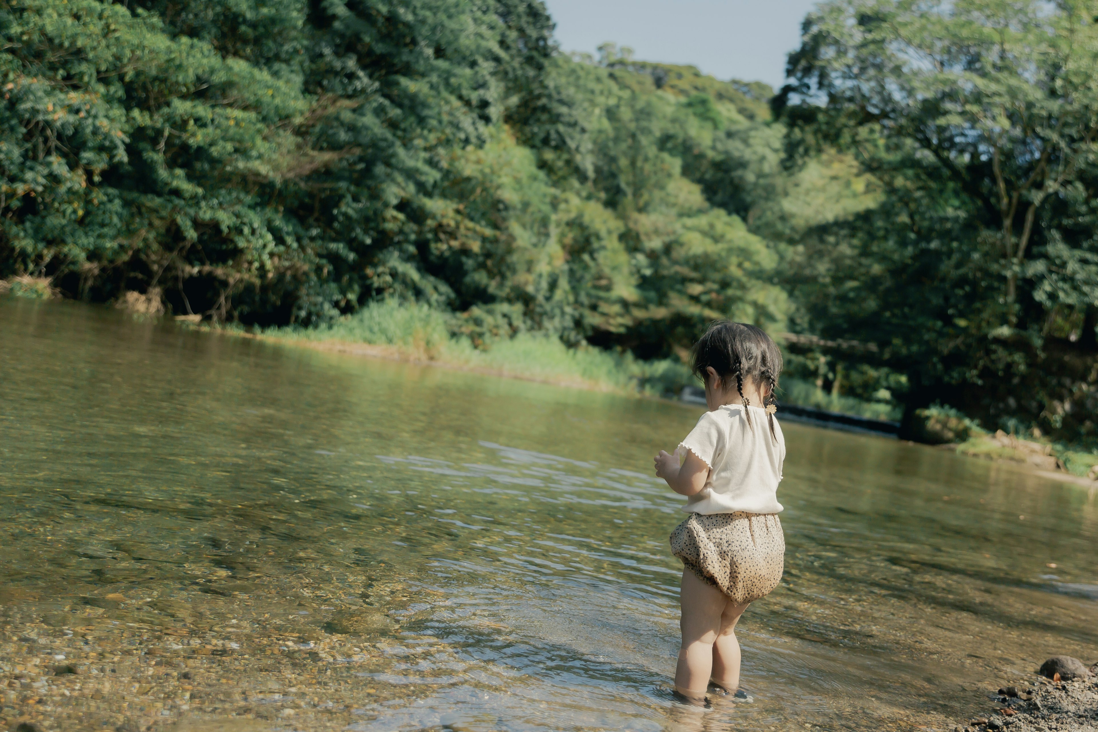 川辺で遊ぶ幼児　緑豊かな風景　水に足を浸す