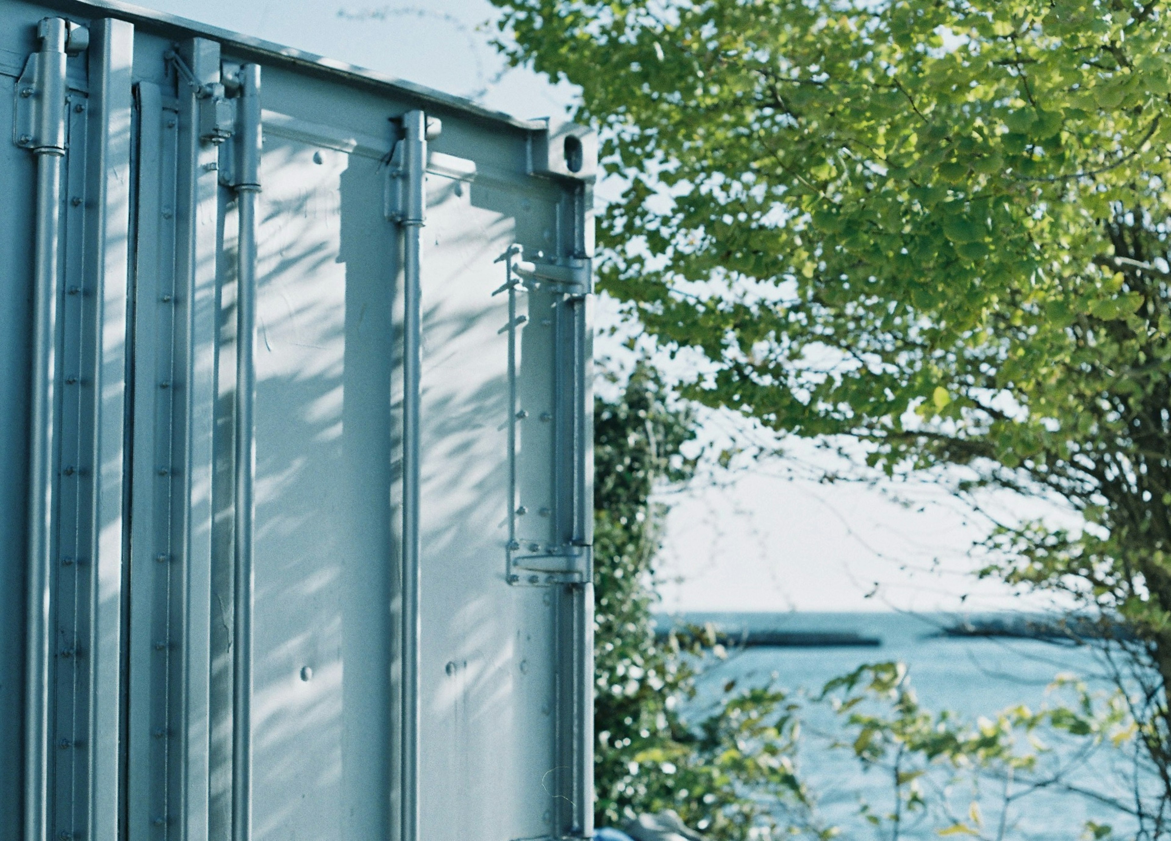 Side view of a metal container with blue sea and green trees in the background