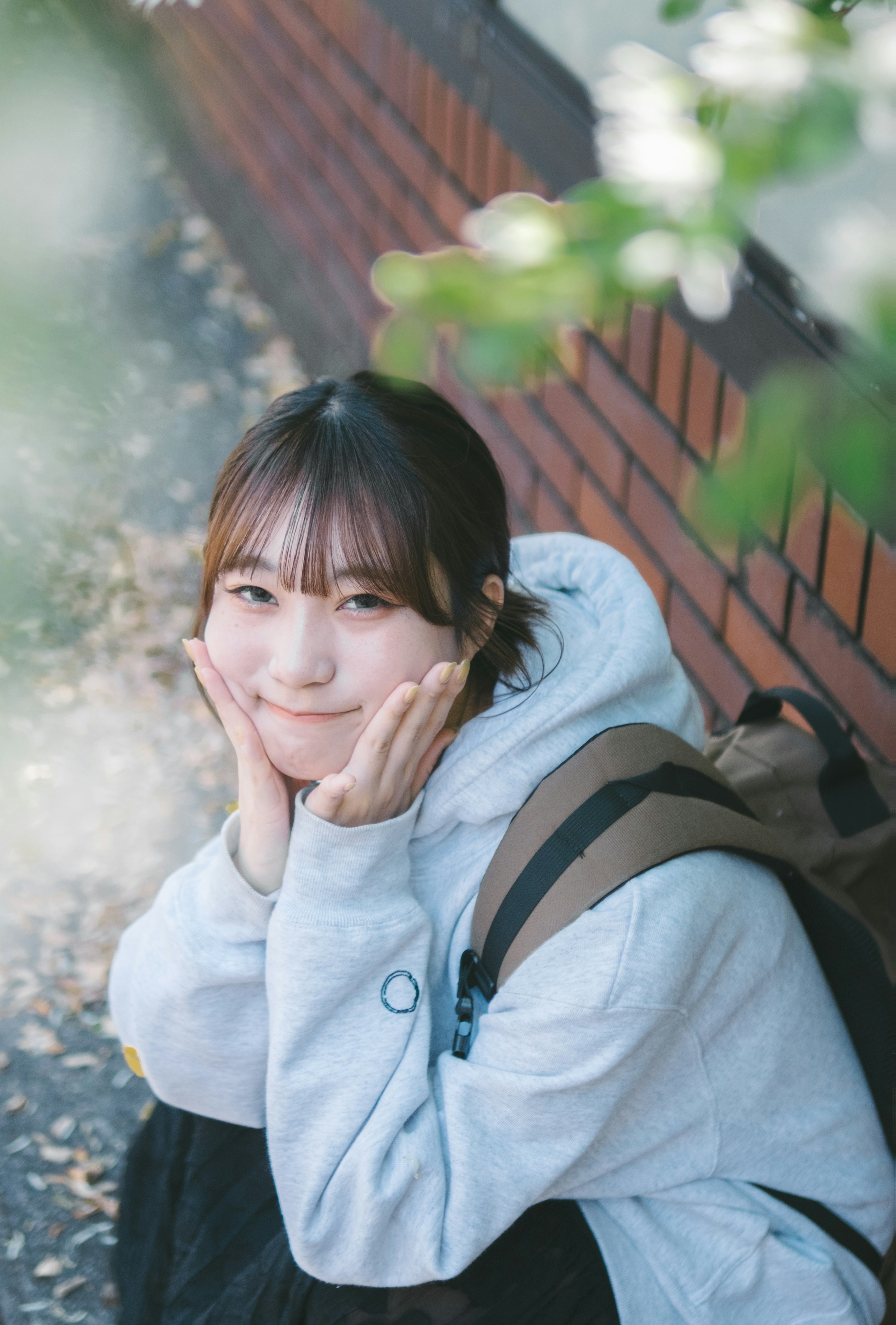 A young woman smiling while resting her chin on her hands surrounded by greenery