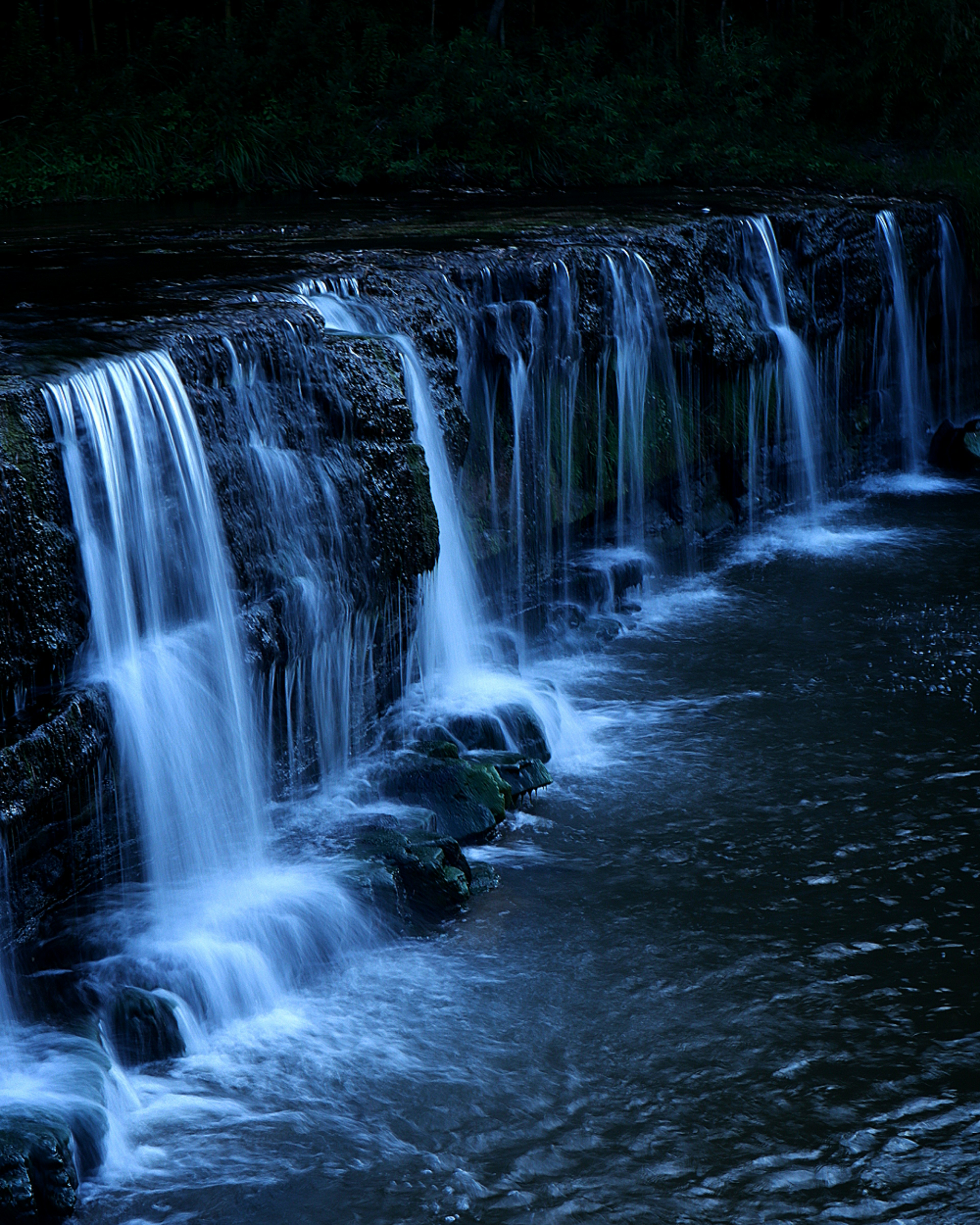 暗い水辺に流れる滝の美しい風景