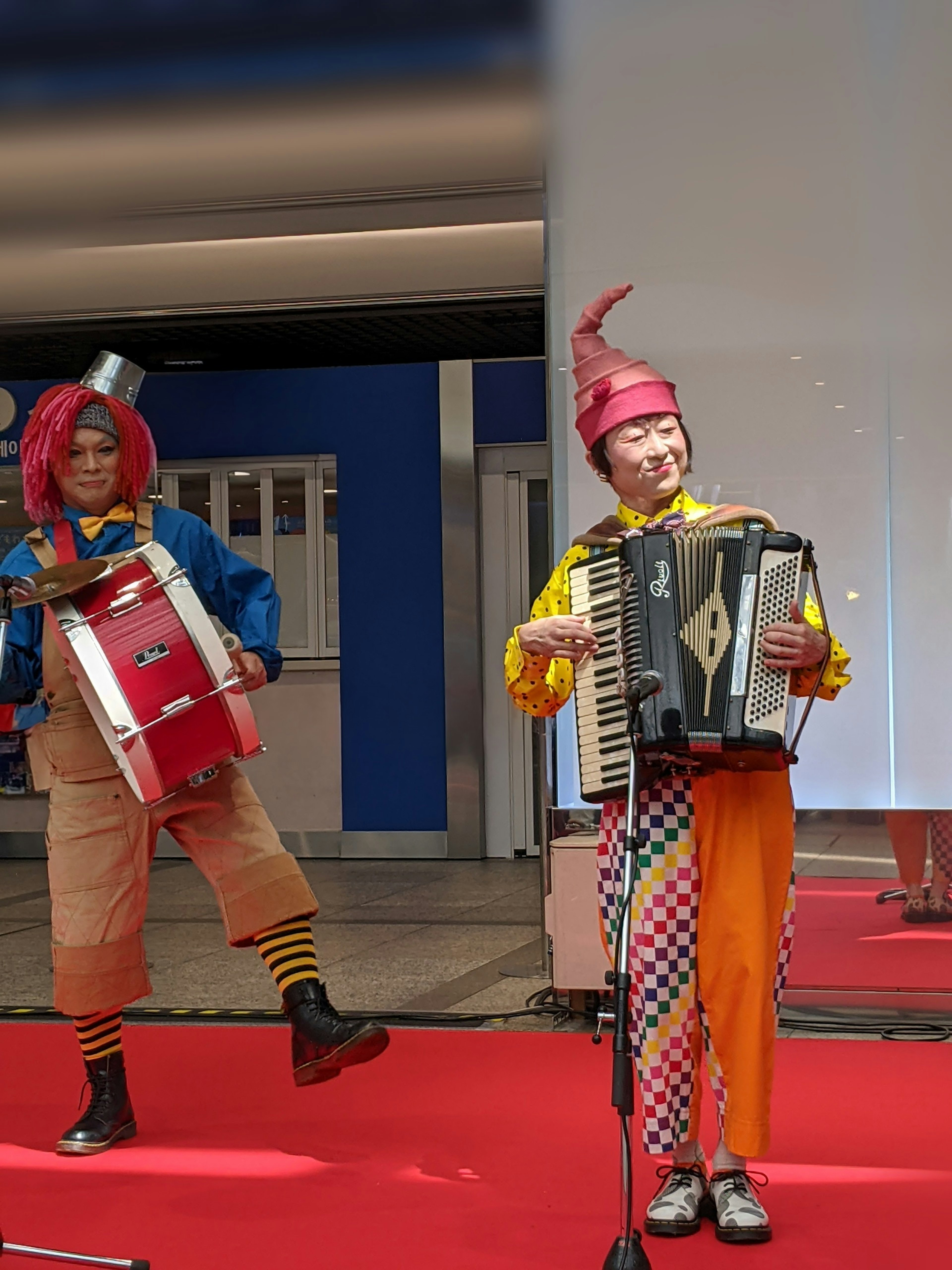 Colorful clowns performing on a red carpet with an accordion and drums