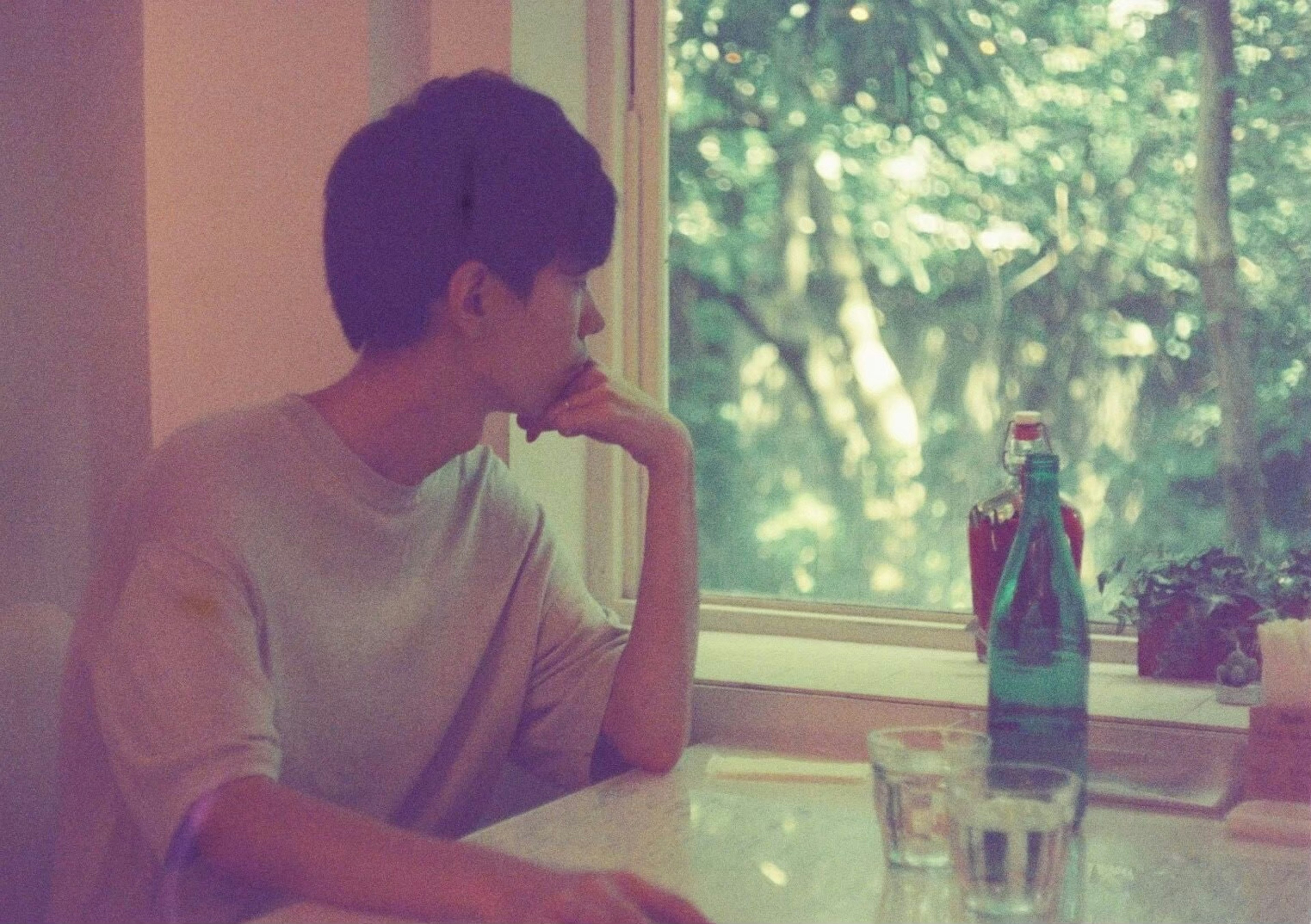 Joven mirando por la ventana con una botella de agua en la mesa