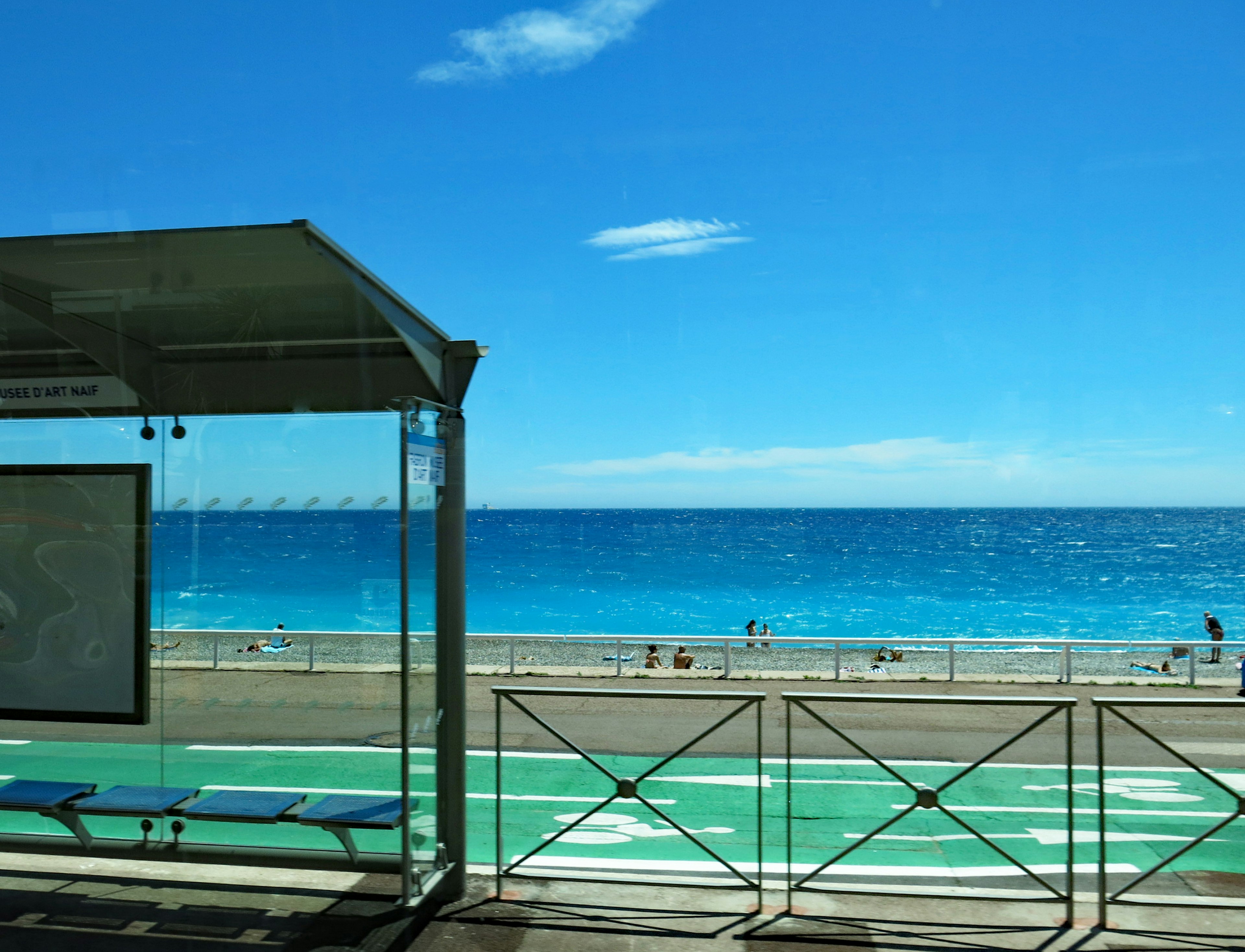 Scena di spiaggia con mare blu e cielo sereno che mostra una fermata dell'autobus e una pista ciclabile