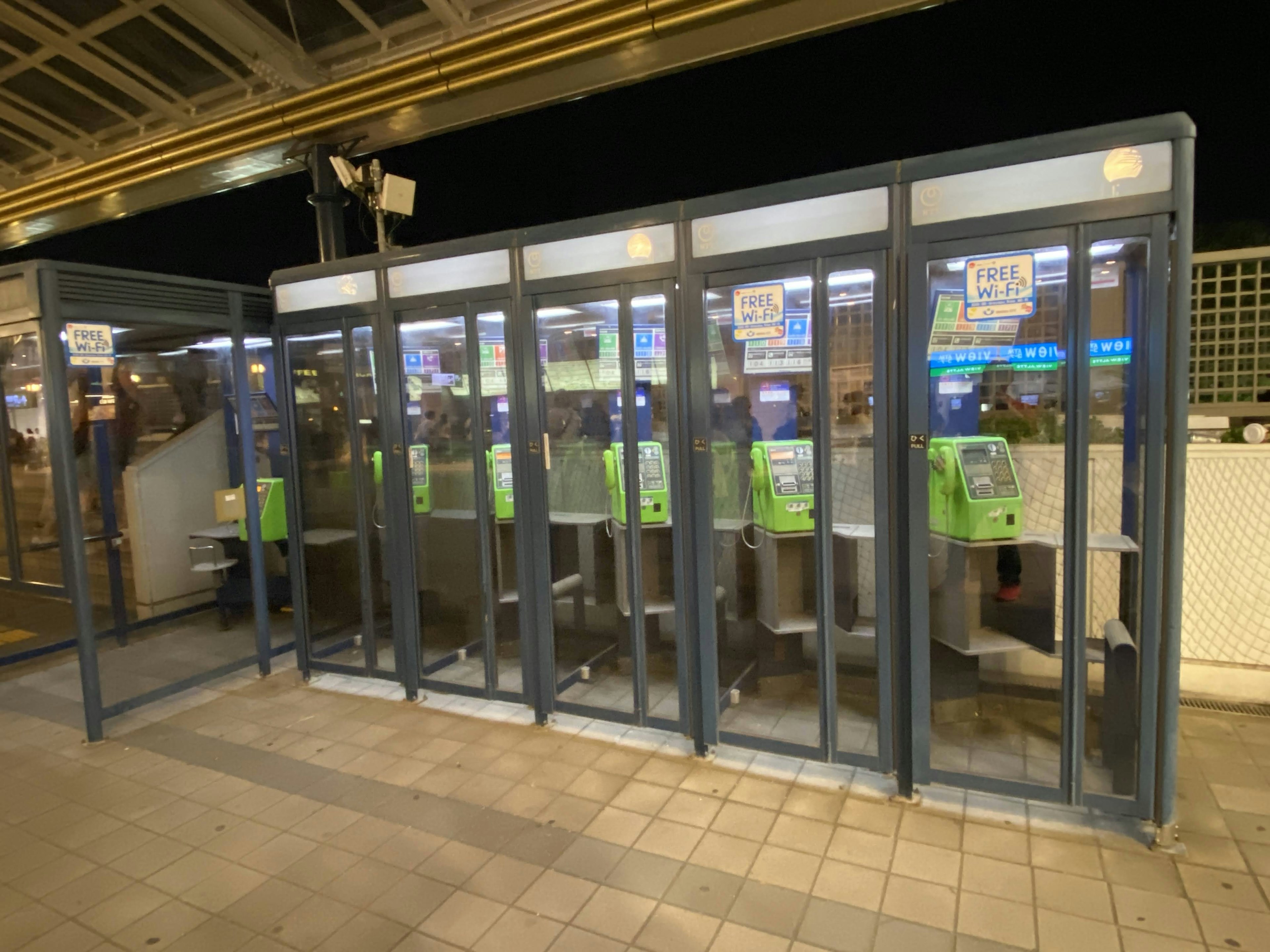 Green ticket vending machines in booths at a train station at night