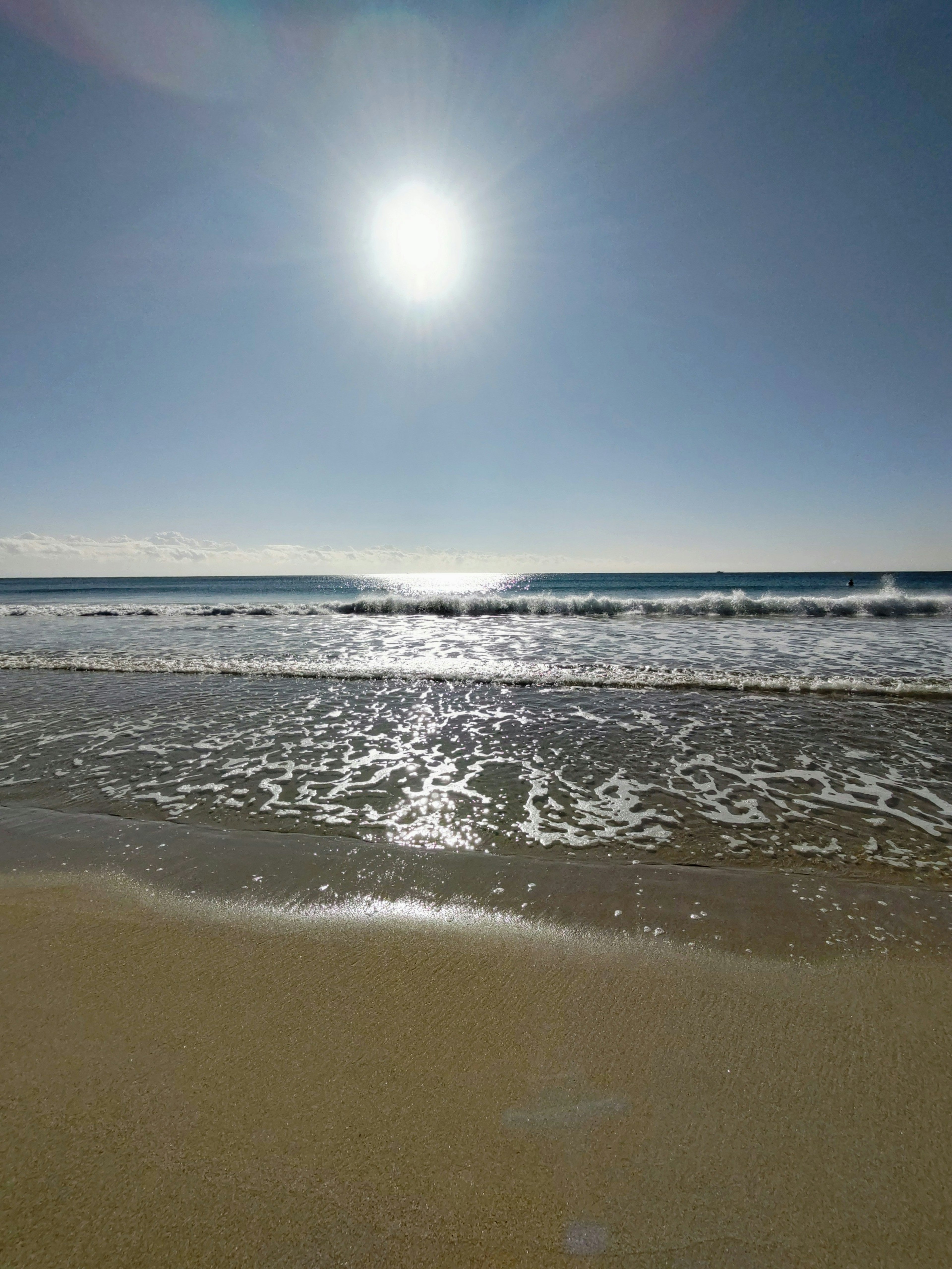 Strandszene mit strahlender Sonne über blauem Ozean und Himmel