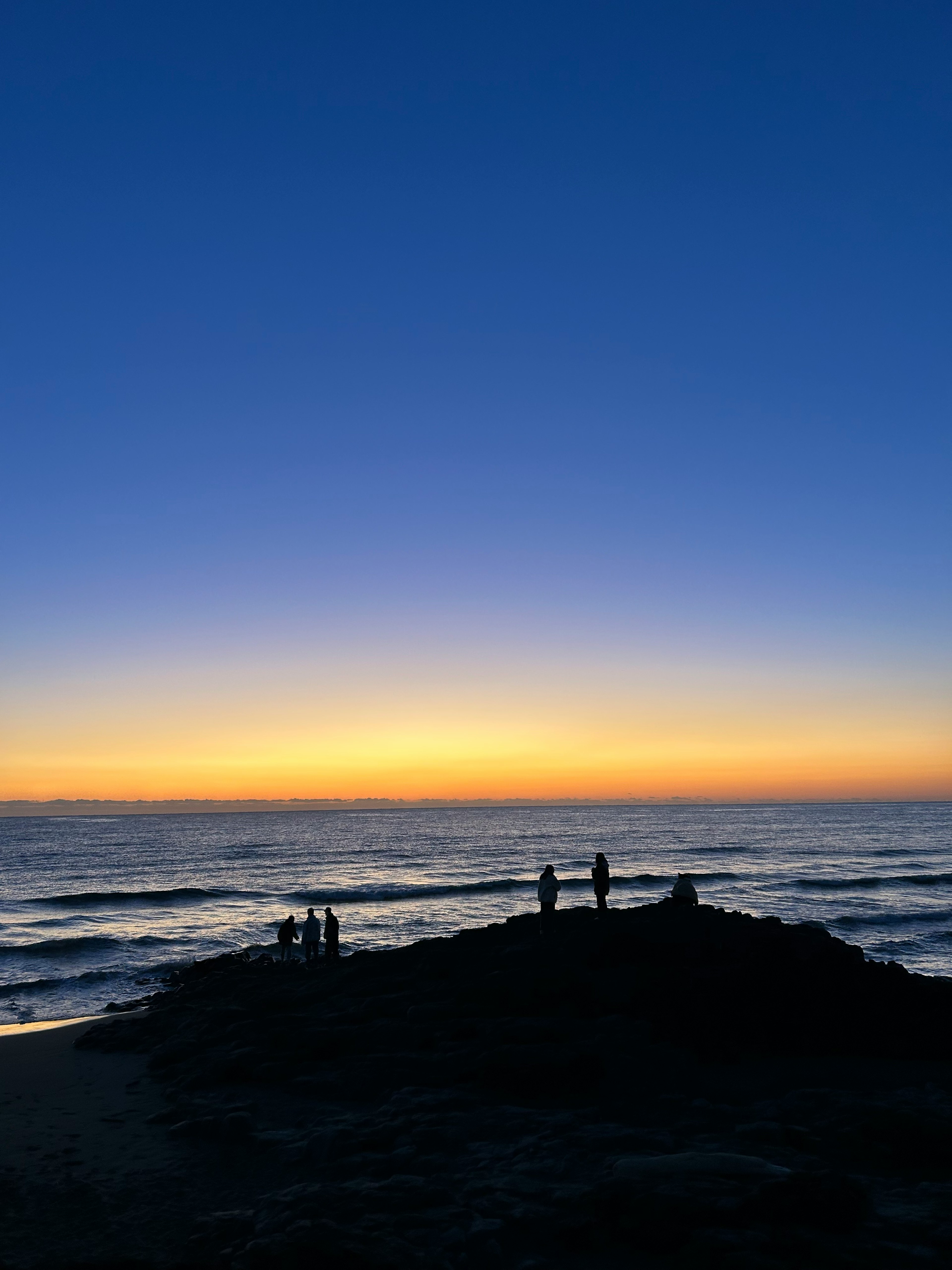 夕日の中で海辺に立つ人々のシルエット