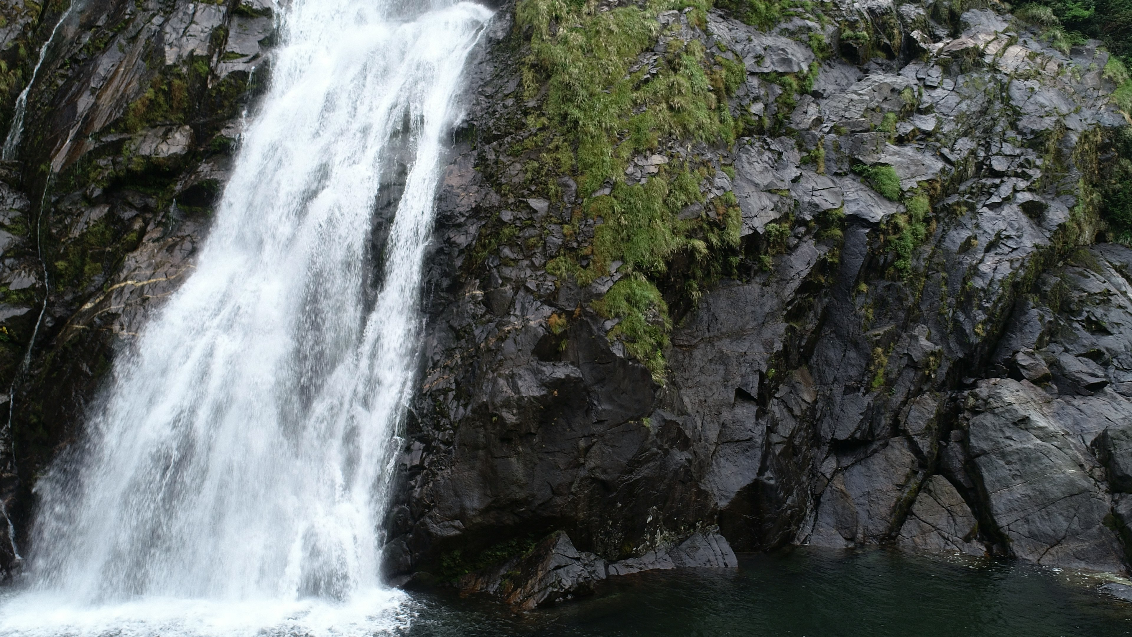 Air terjun yang indah mengalir dari tebing berbatu dikelilingi oleh pepohonan hijau