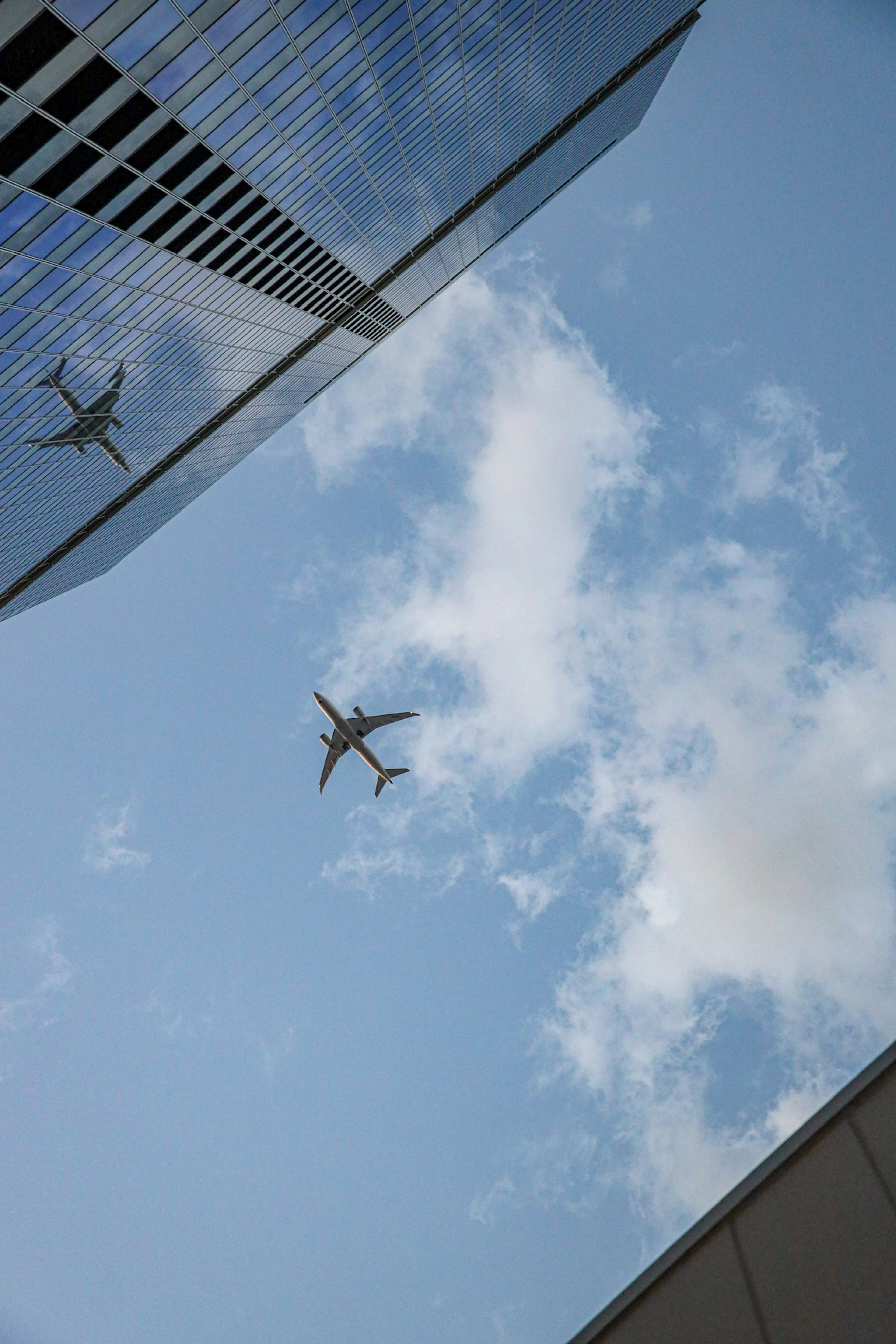 高層ビルの反射と空を背景に飛行機が飛んでいる