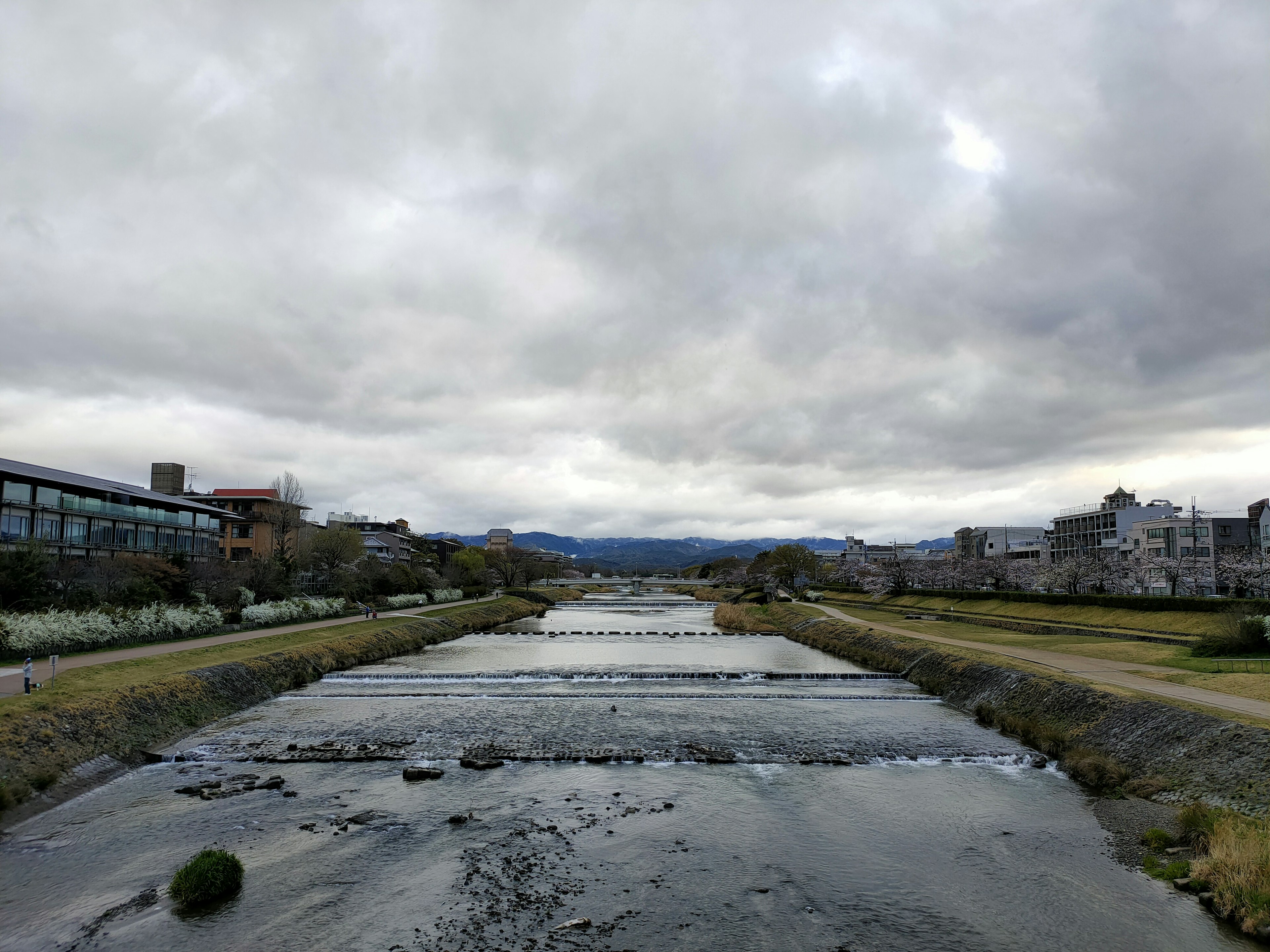 静かな川と曇り空の風景 川の両側には緑の草地と建物が見える