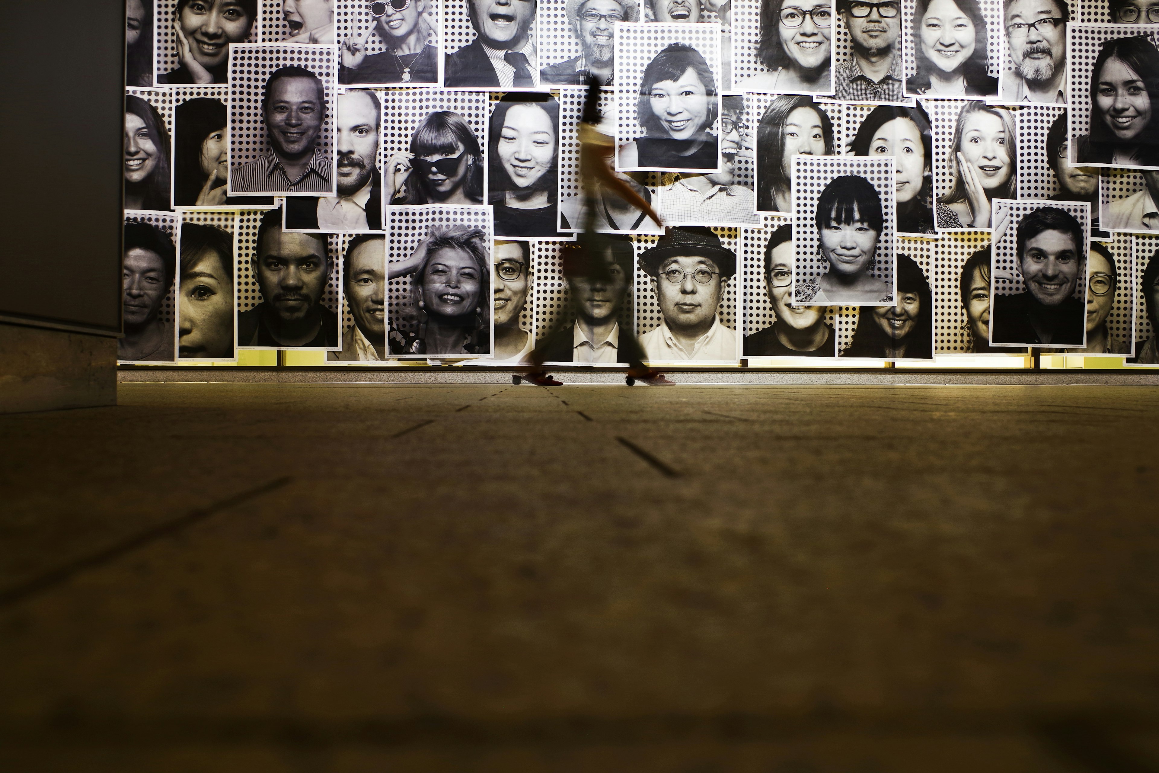 Una persona caminando frente a una pared cubierta de numerosos retratos