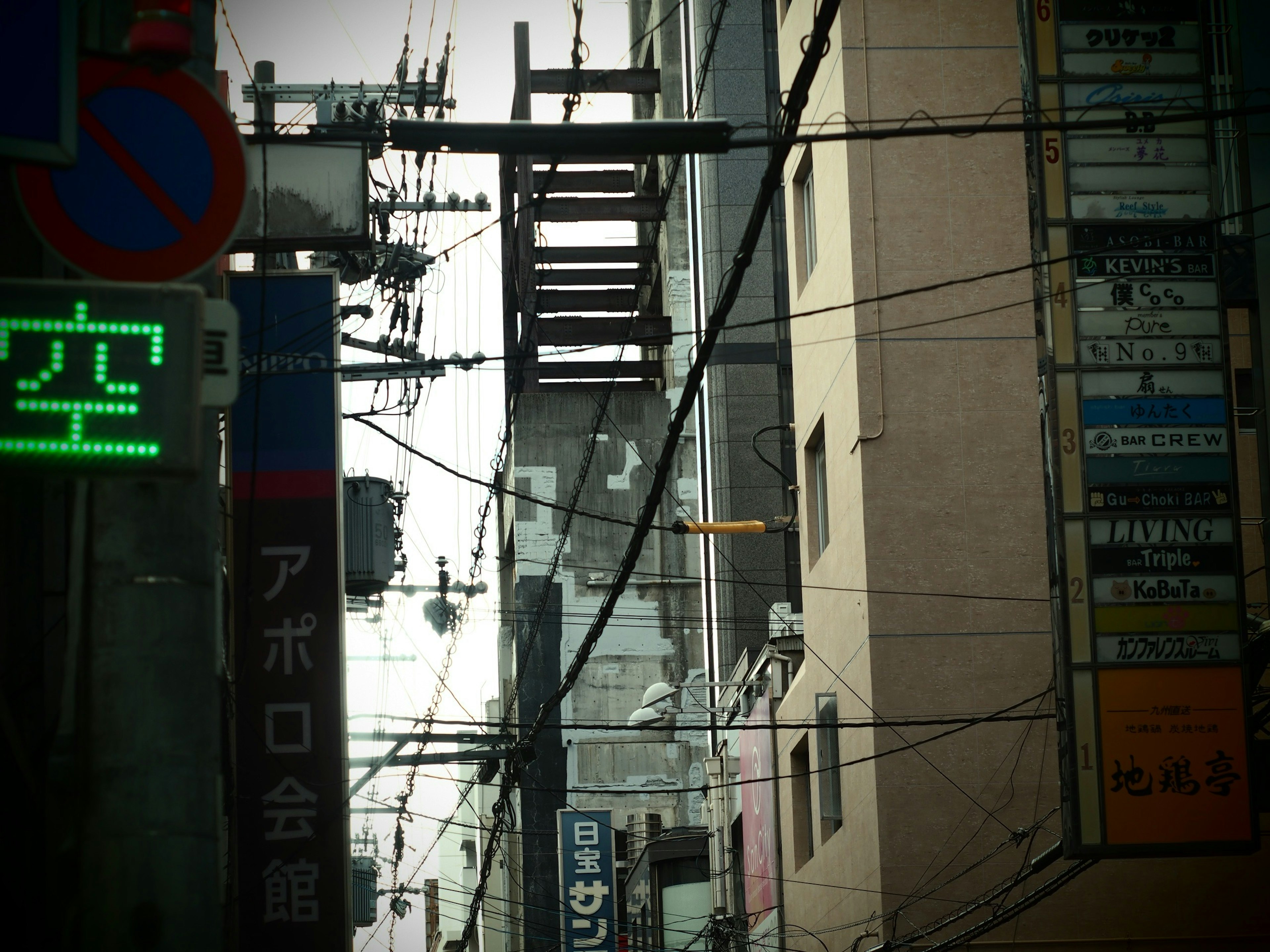 Scène urbaine avec des lignes électriques et des bâtiments affichant un panneau vert et du texte japonais