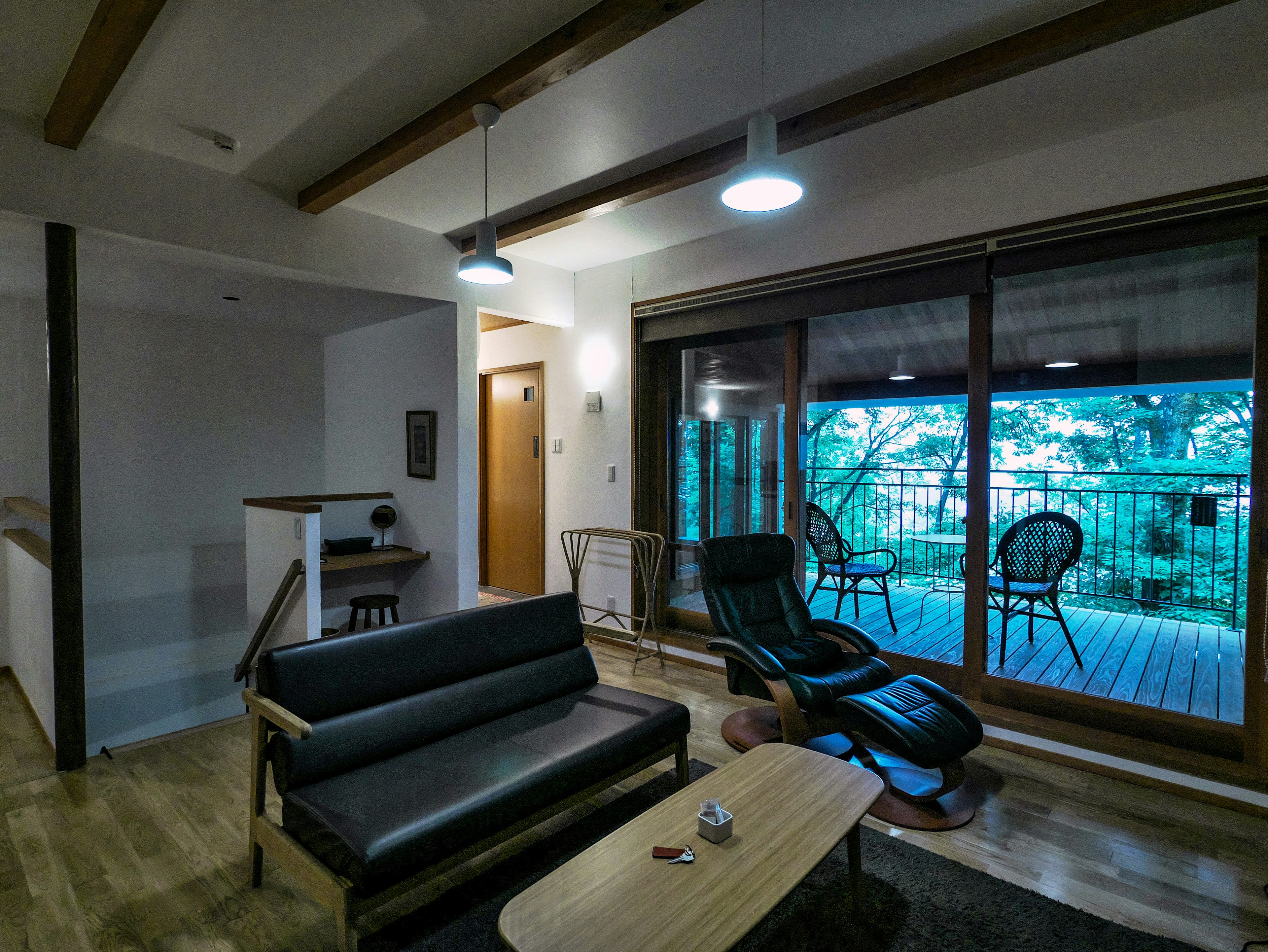 Modern living room interior featuring a black sofa two chairs and a coffee table with a large window showing a green view