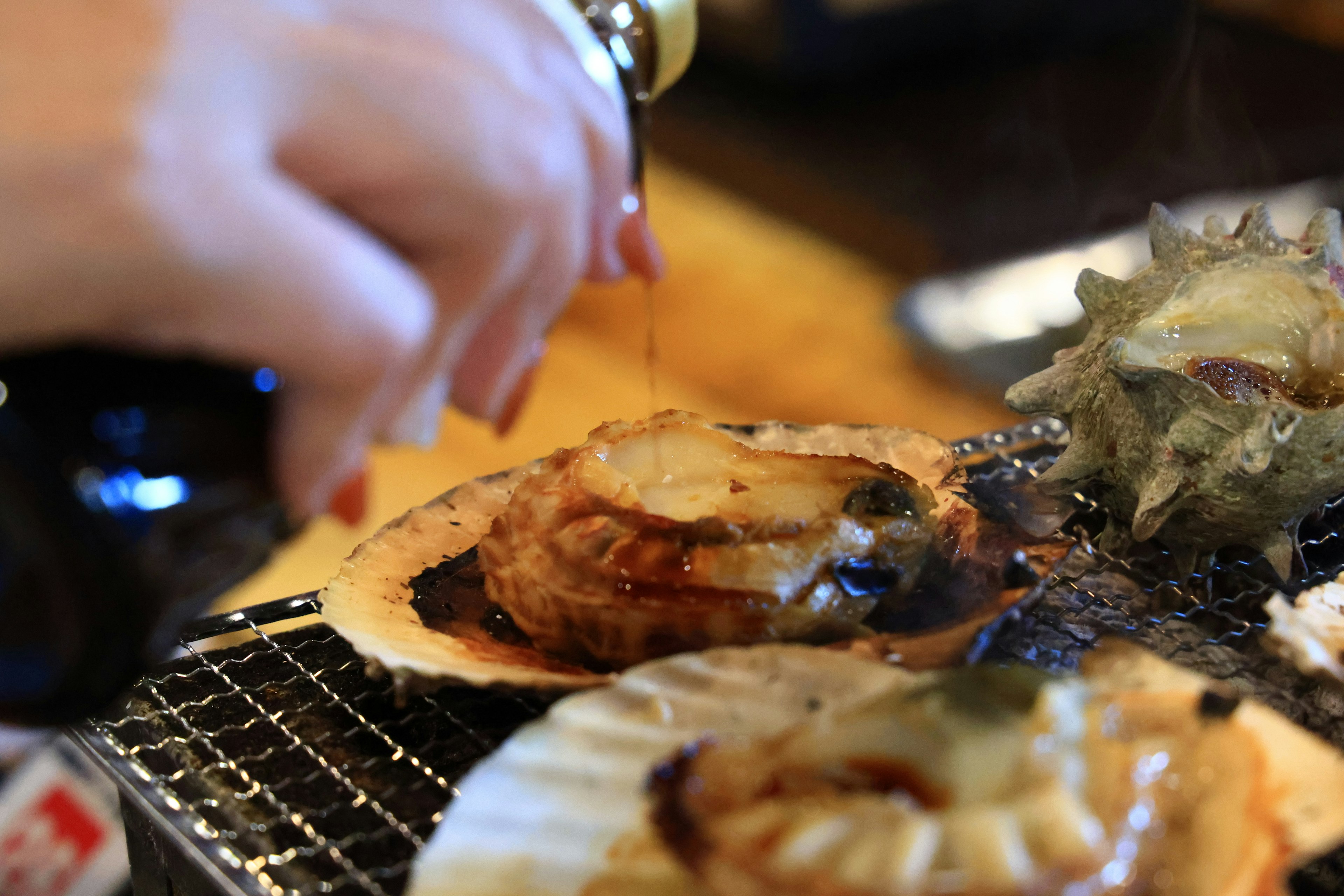 Mano vertiendo salsa sobre vieiras y mariscos a la parrilla