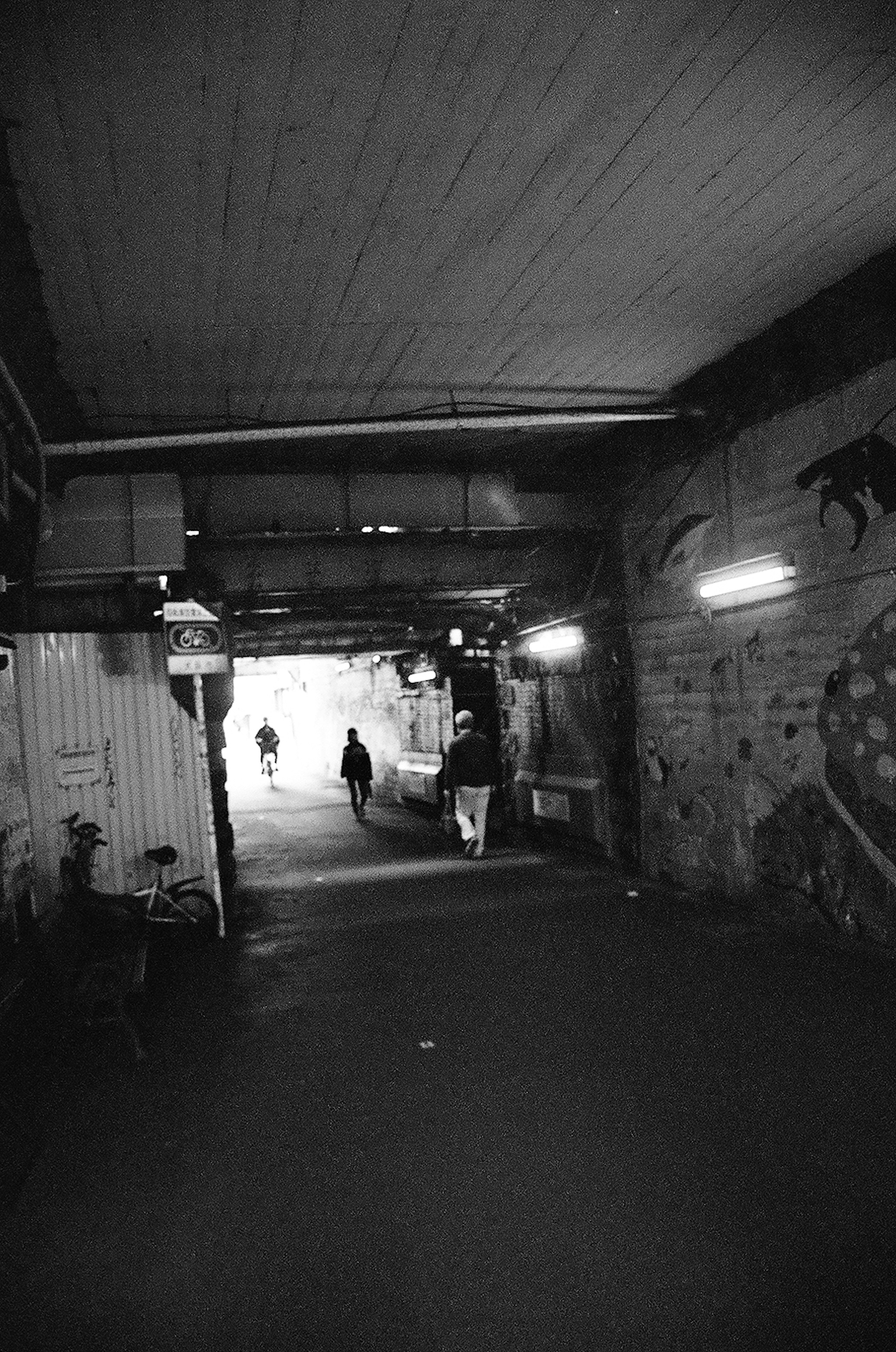 Silhouettes of people walking through a dark tunnel with graffiti on the walls