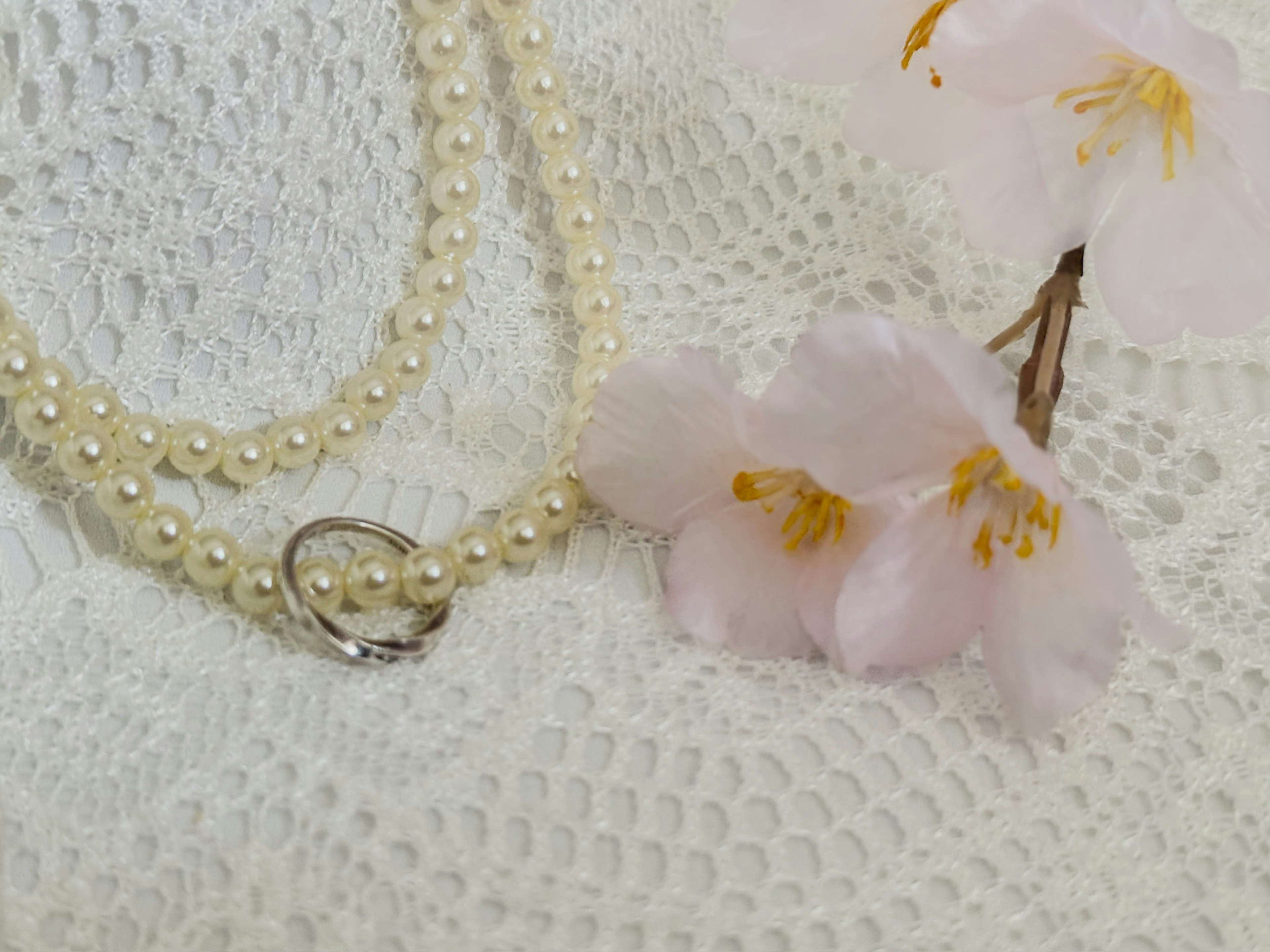 A pearl necklace and cherry blossom flowers arranged on a white lace background