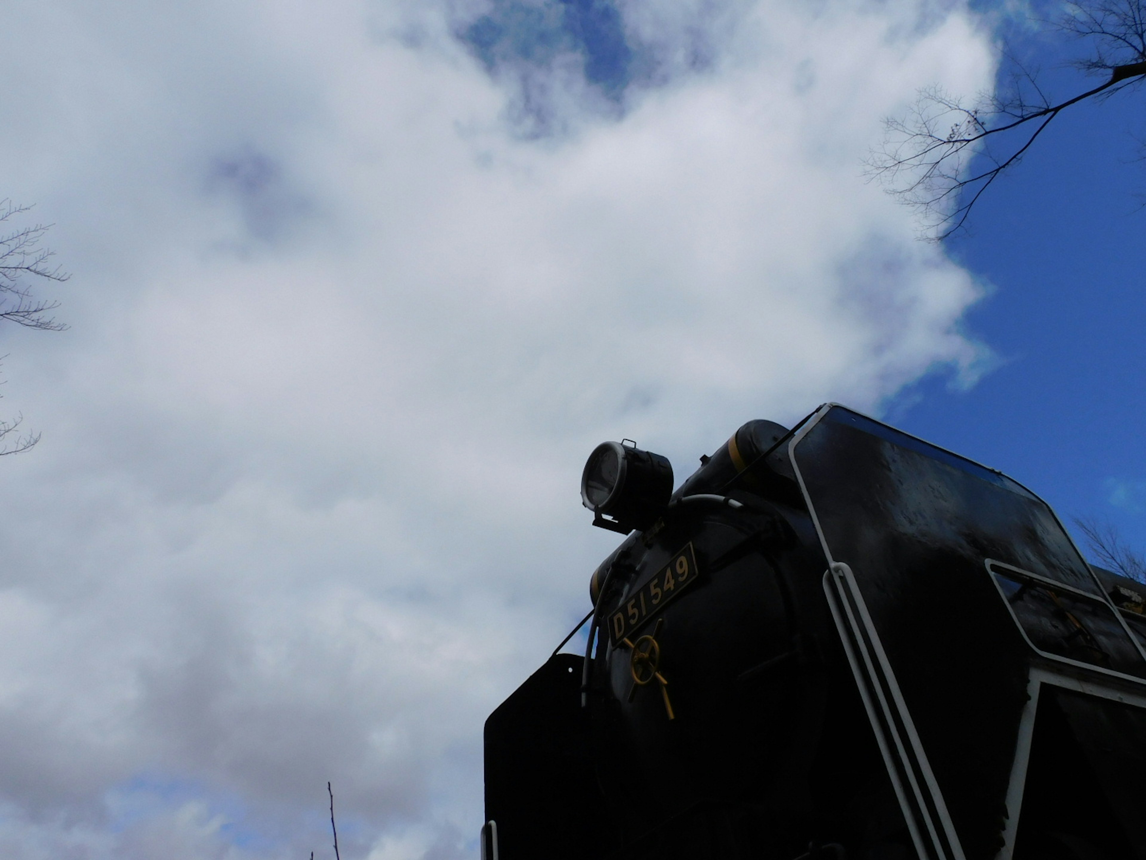 Part of an old steam locomotive against a backdrop of blue sky and clouds