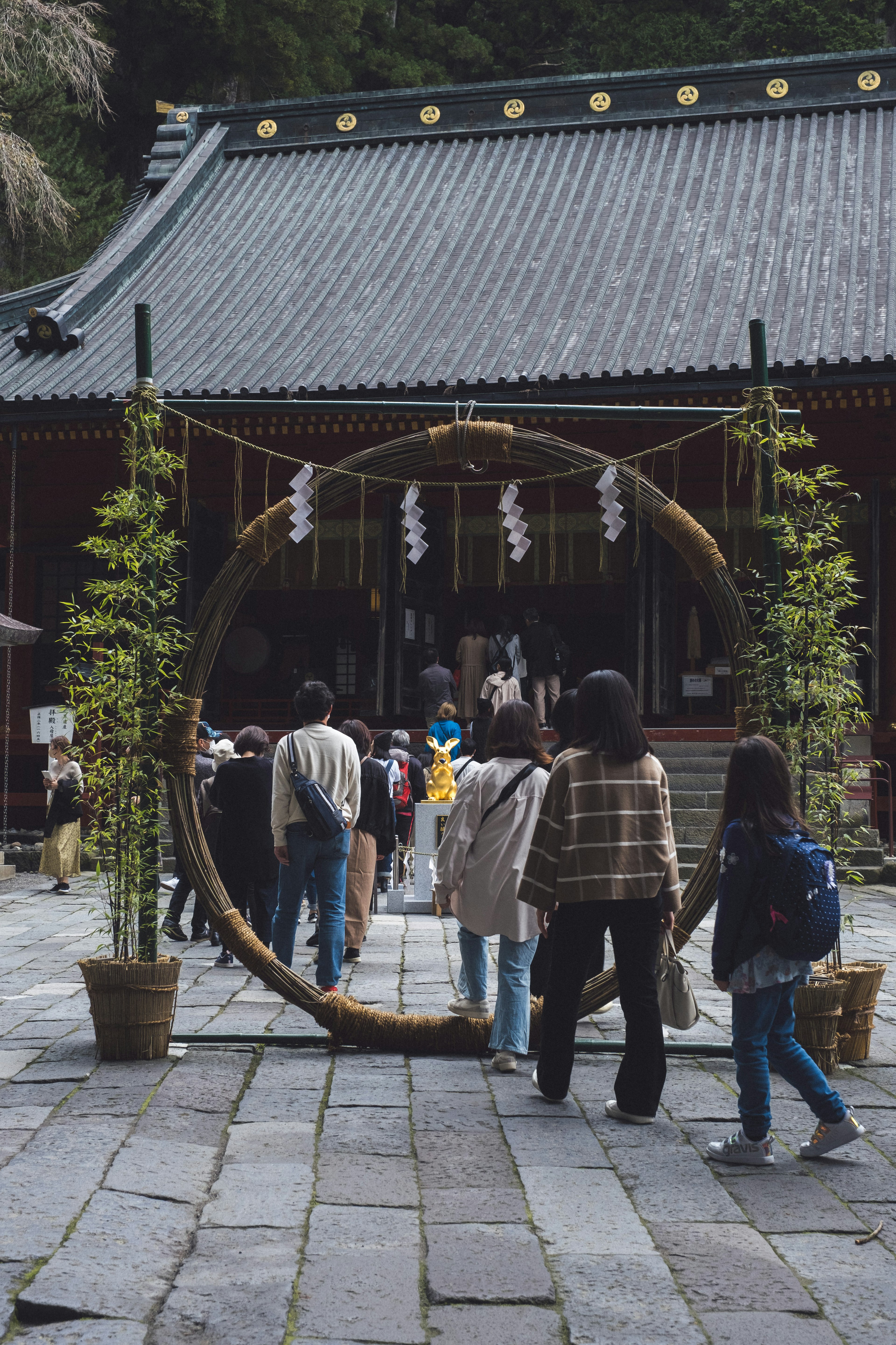 参拝者が大きな輪をくぐって神社に向かう様子と伝統的な建物