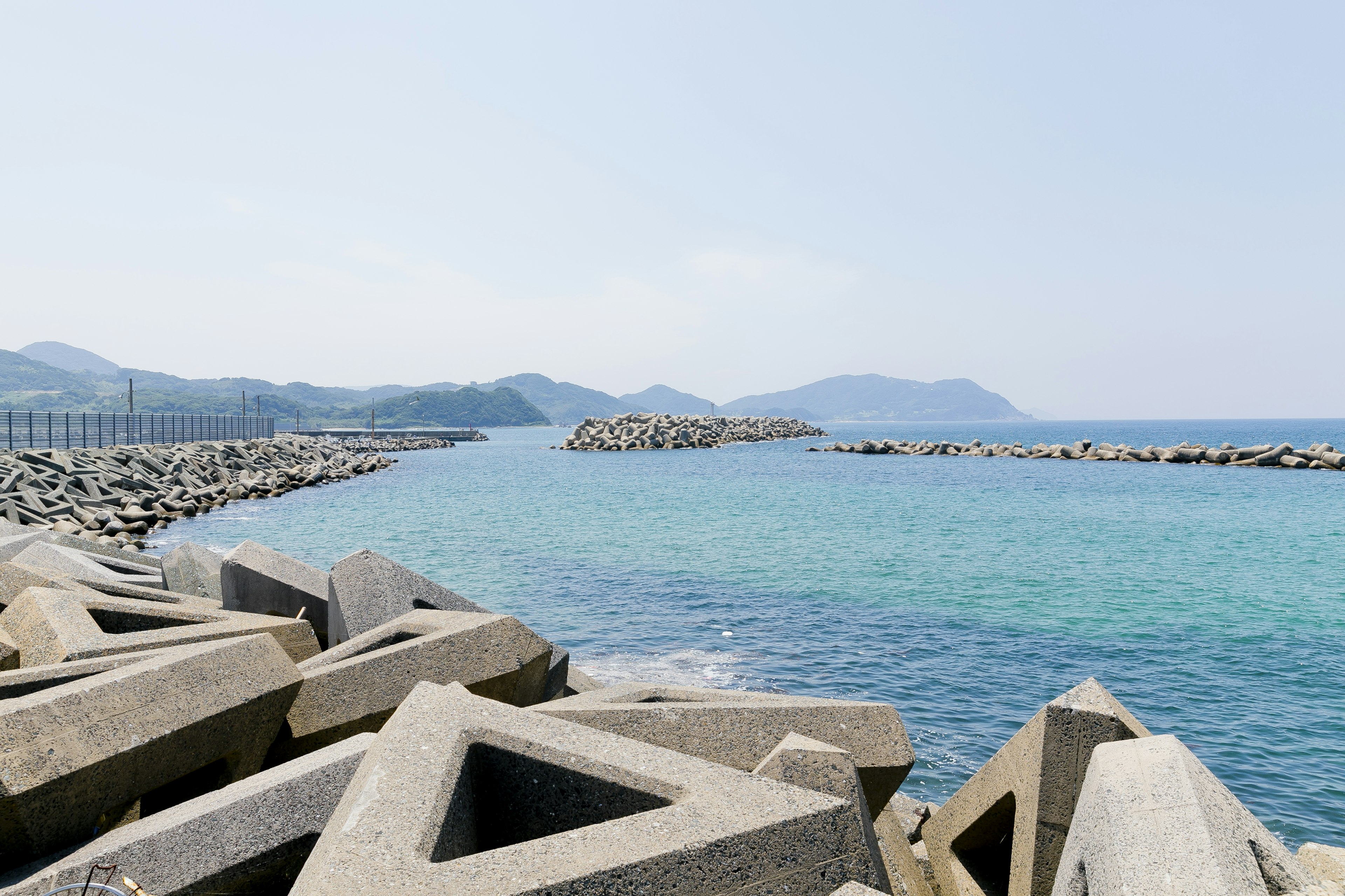 Vista escénica del mar azul con un rompeolas de concreto y montañas distantes