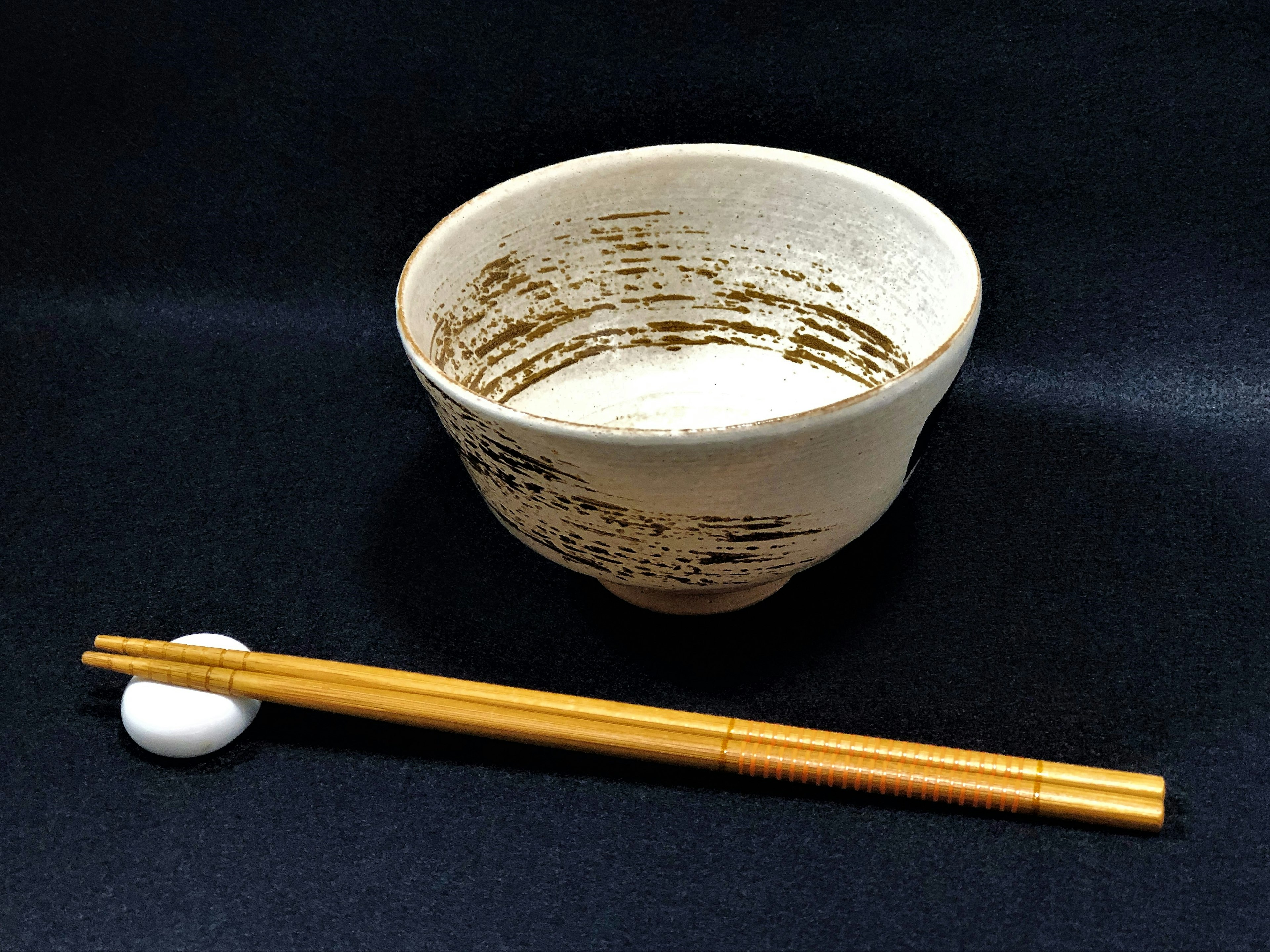 A white ceramic bowl with a textured design next to bamboo chopsticks on a black background