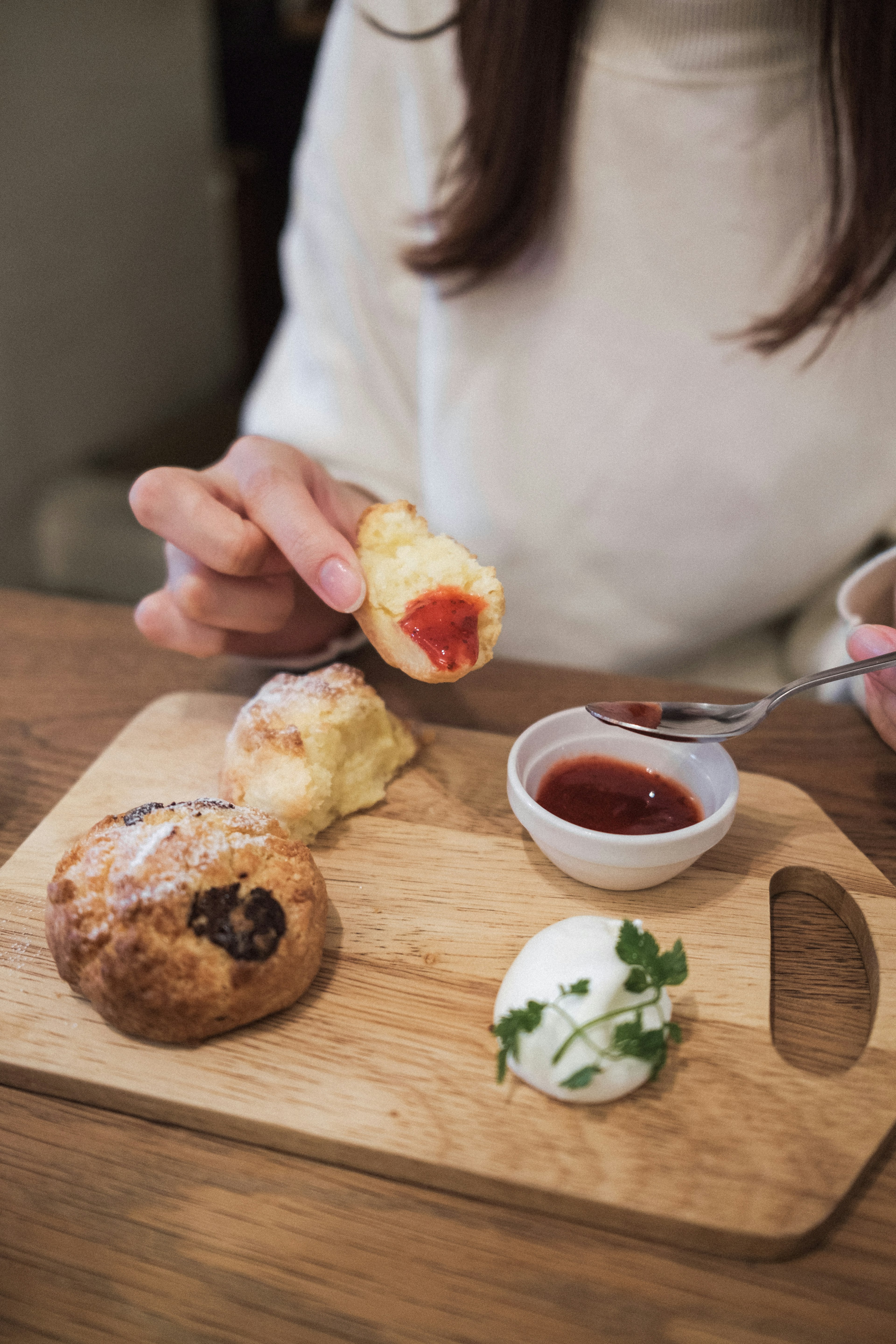 Une main tenant une pâtisserie avec de la confiture et de la crème sur un plateau en bois