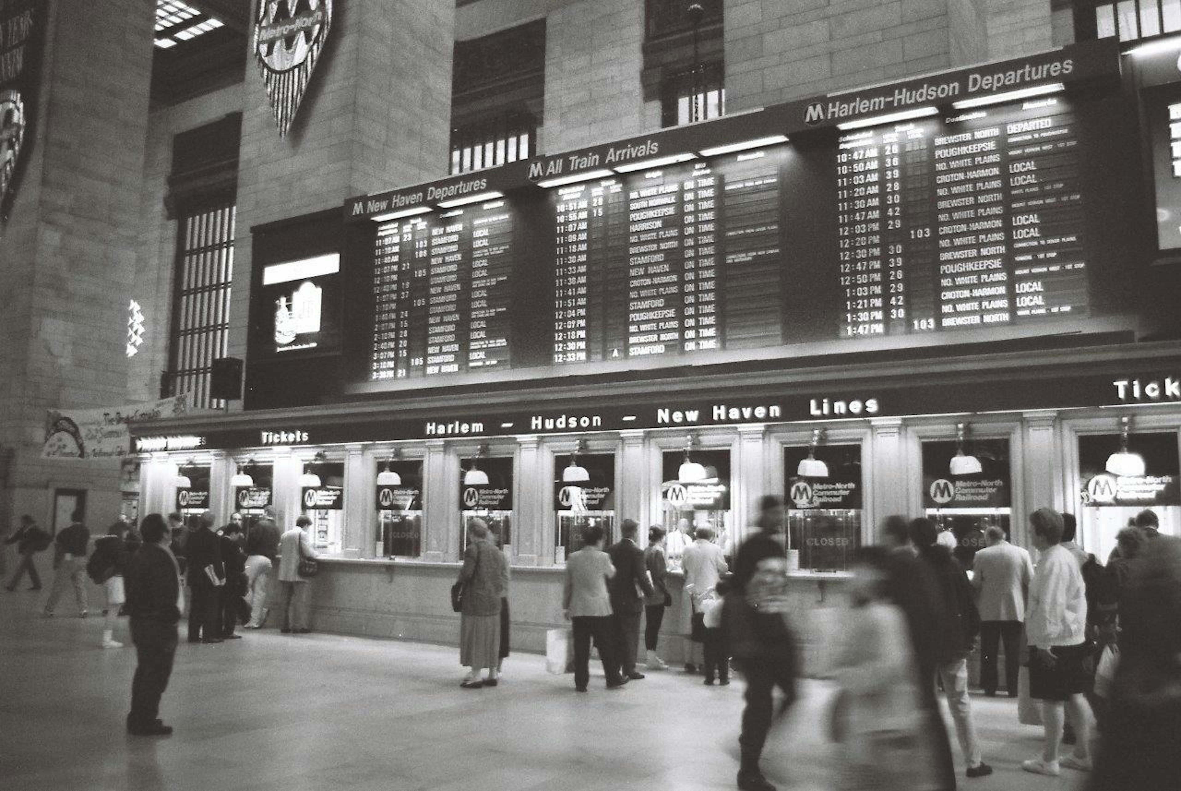 Photo en noir et blanc de la gare Grand Central avec des guichets et un tableau des départs