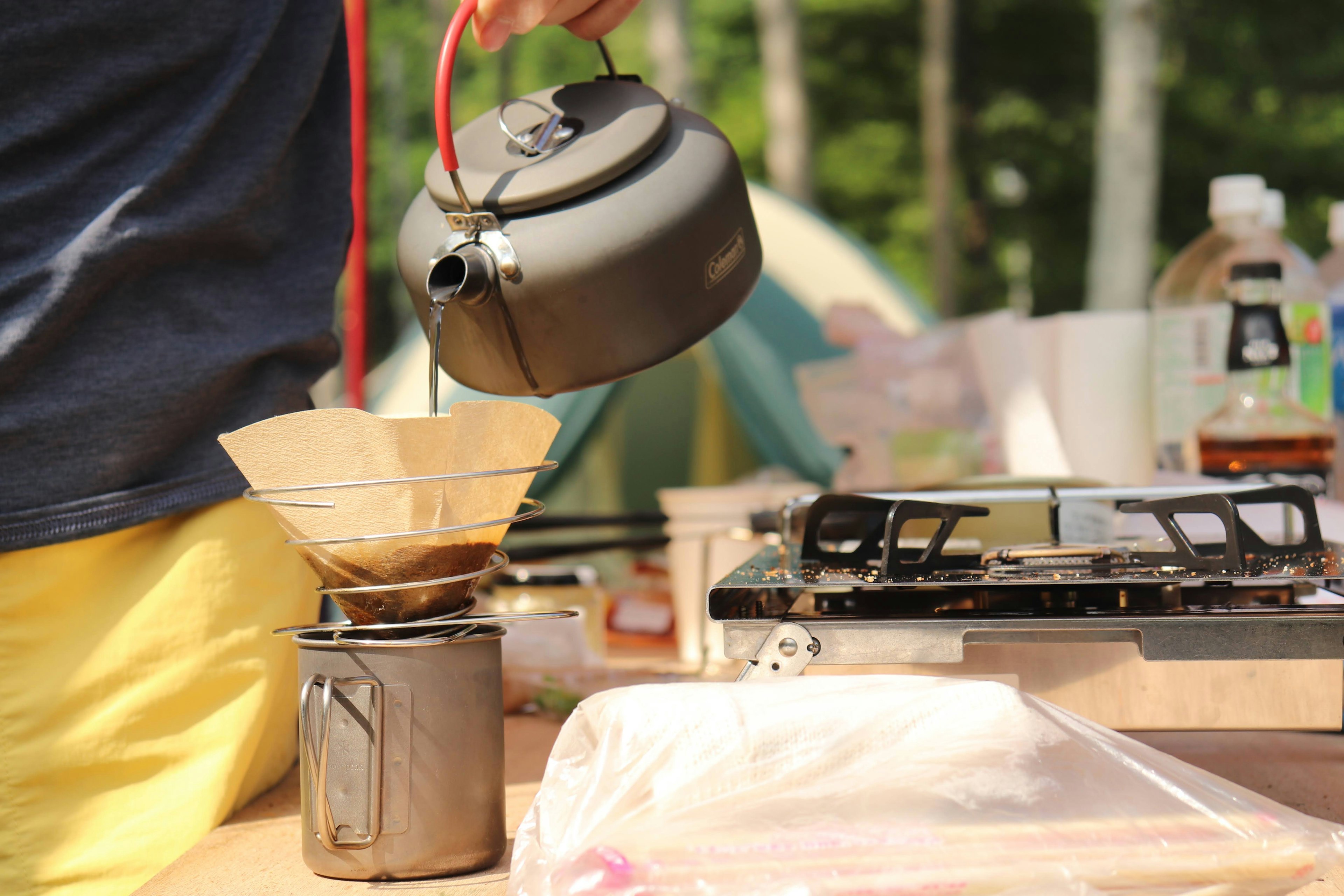 Preparazione del caffè in un campeggio con un kettle nero che versa in un filtro per caffè