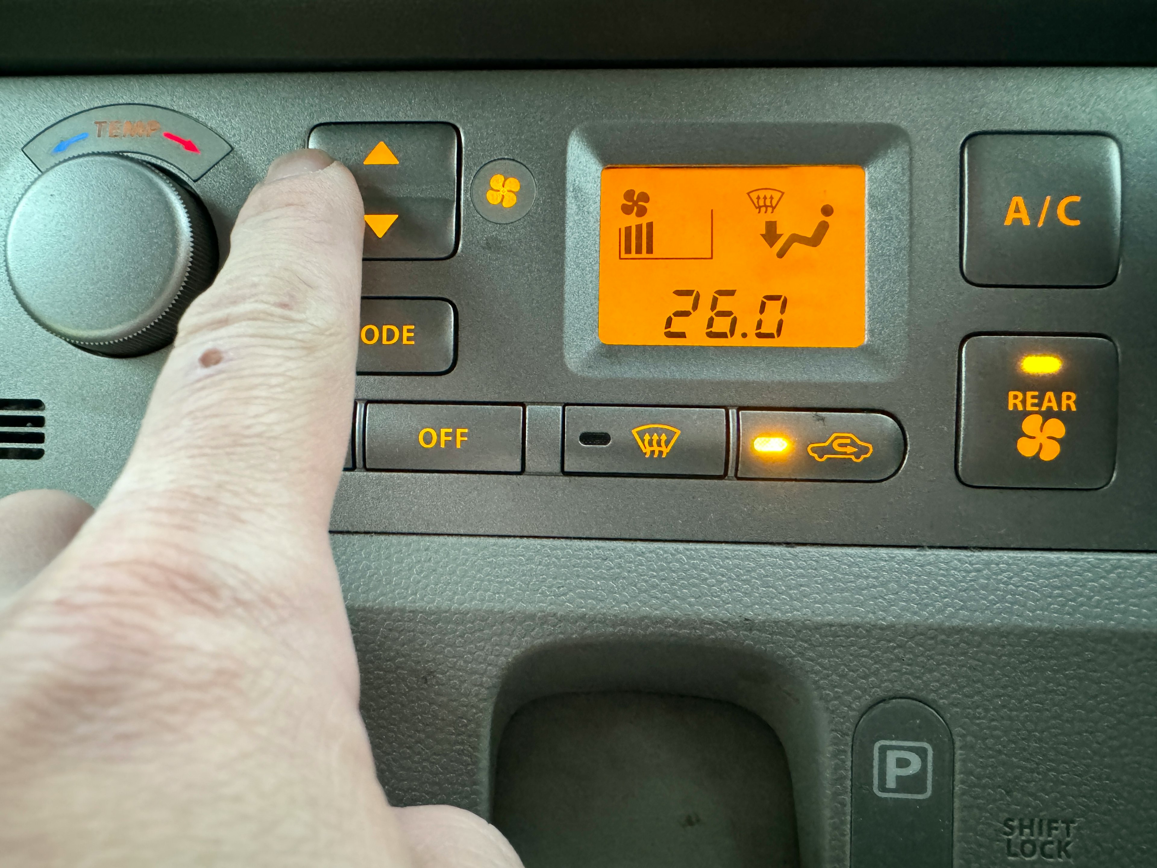 Imagen de un panel de aire acondicionado de automóvil con una mano ajustando la configuración temperatura establecida en 26,0 grados pantalla naranja