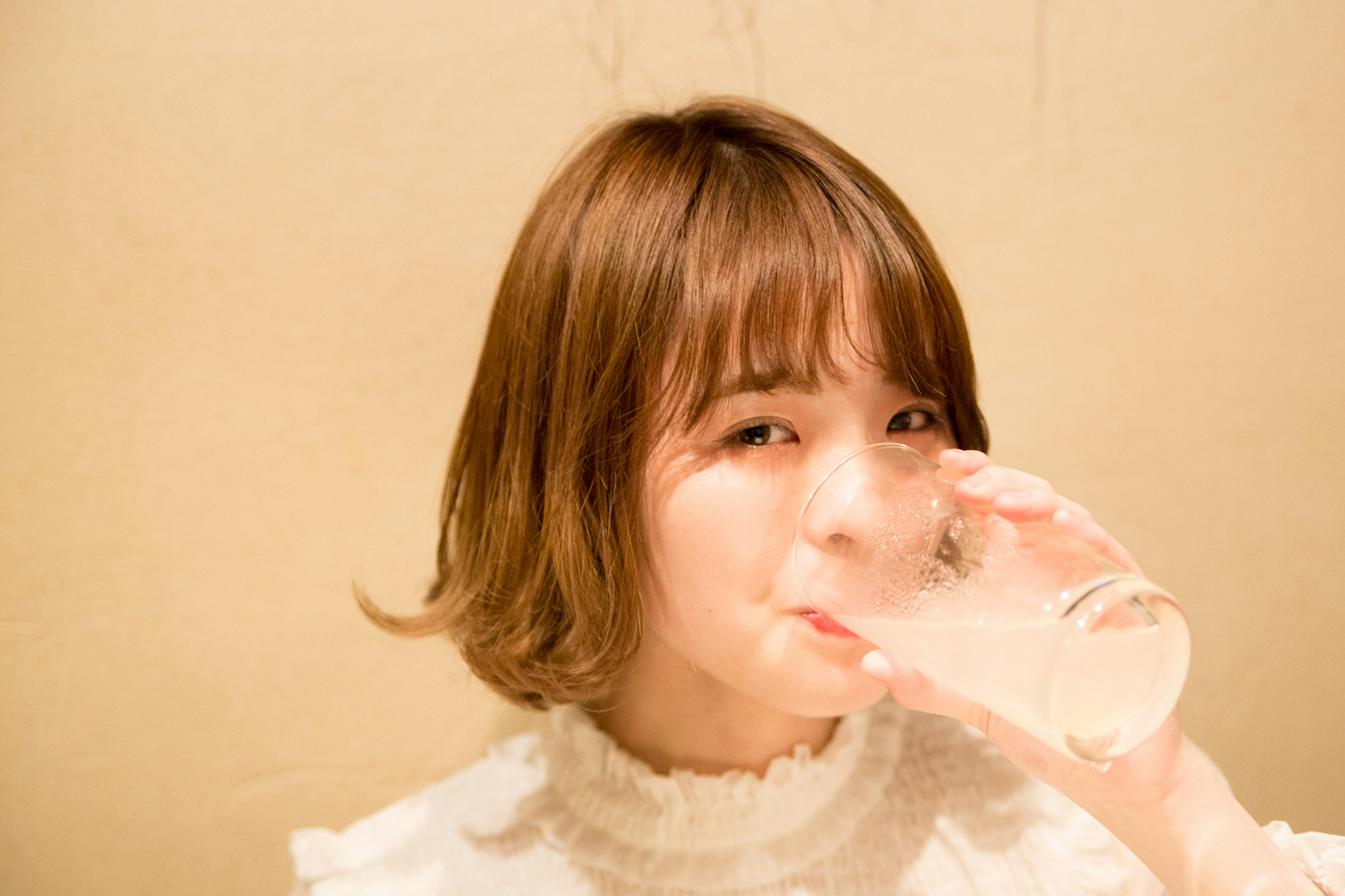 A woman drinking a beverage with a cute hairstyle and a white blouse