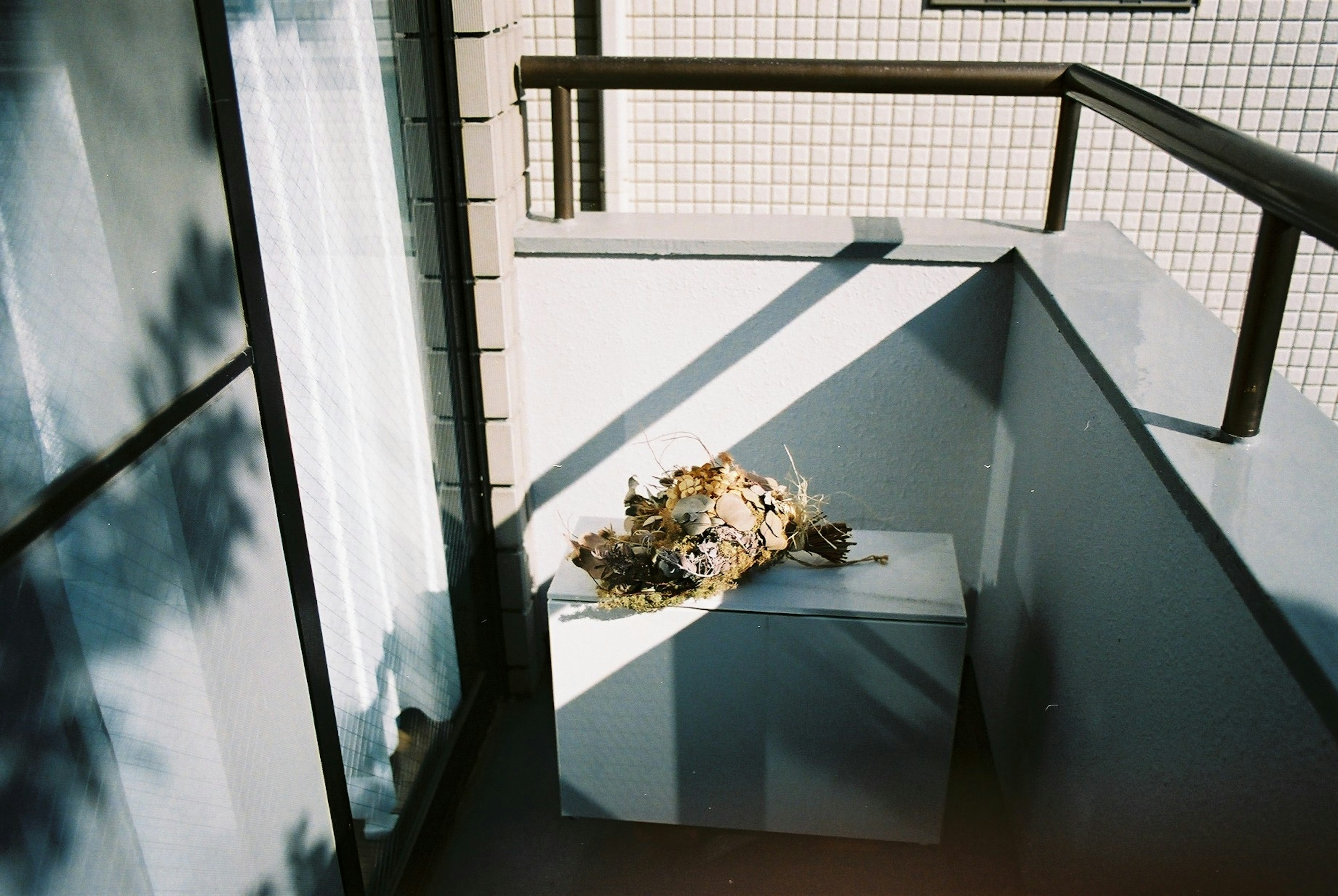 A white box on a balcony with a plant arrangement on top