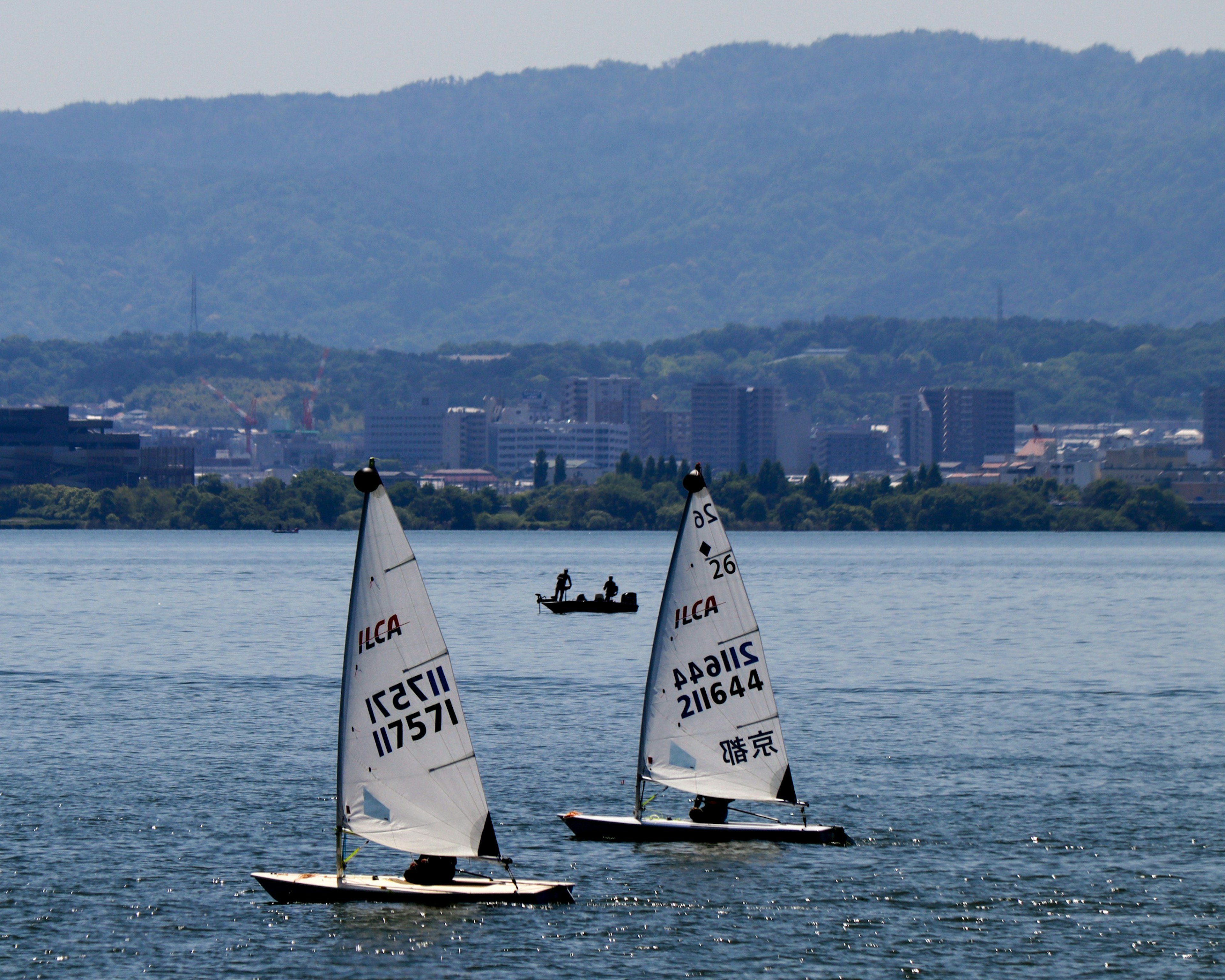 Two sailboats on a lake with a small boat in the background