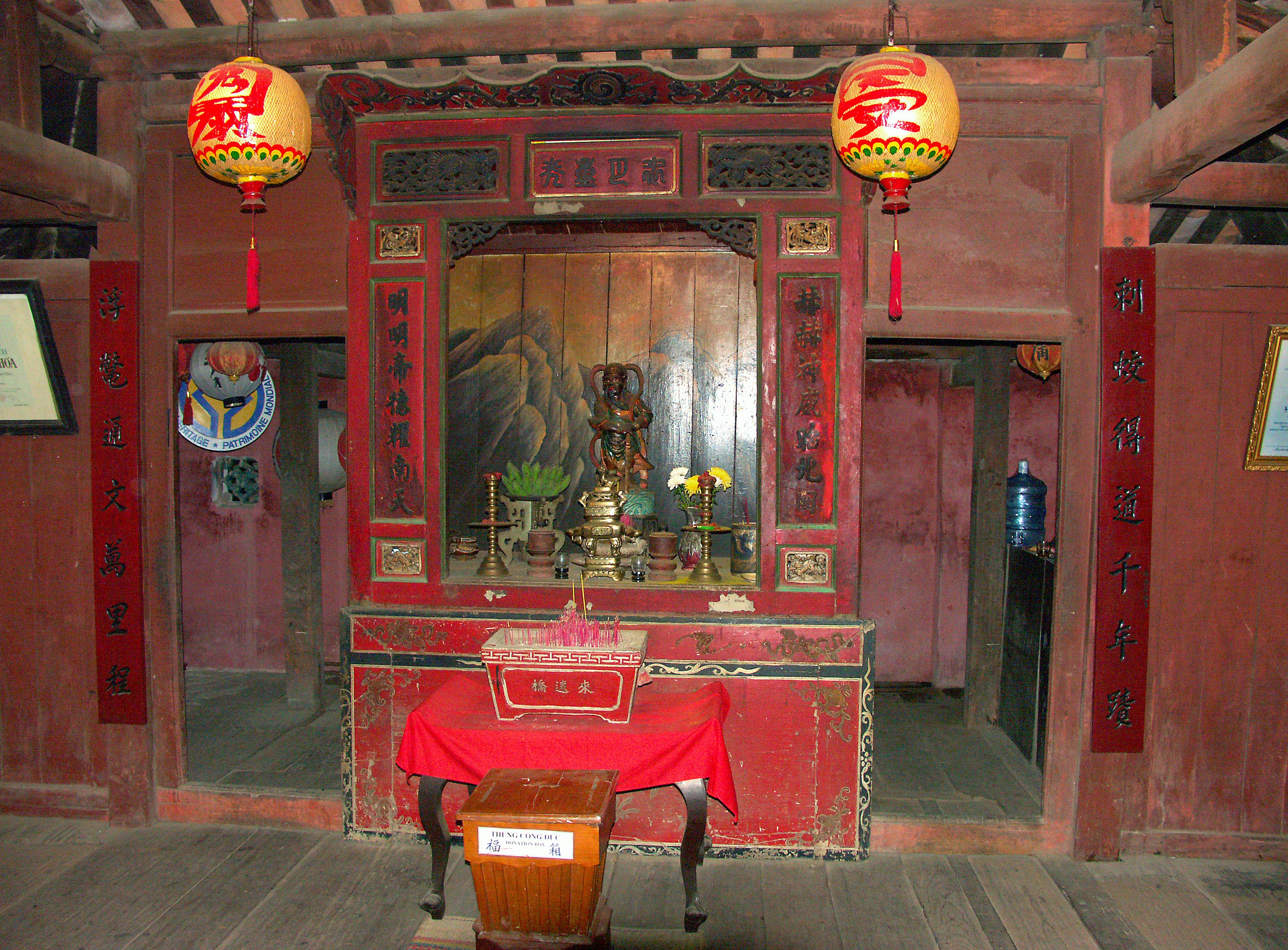 Interior of a shrine with red decorations and offerings on the altar lanterns hanging from the ceiling