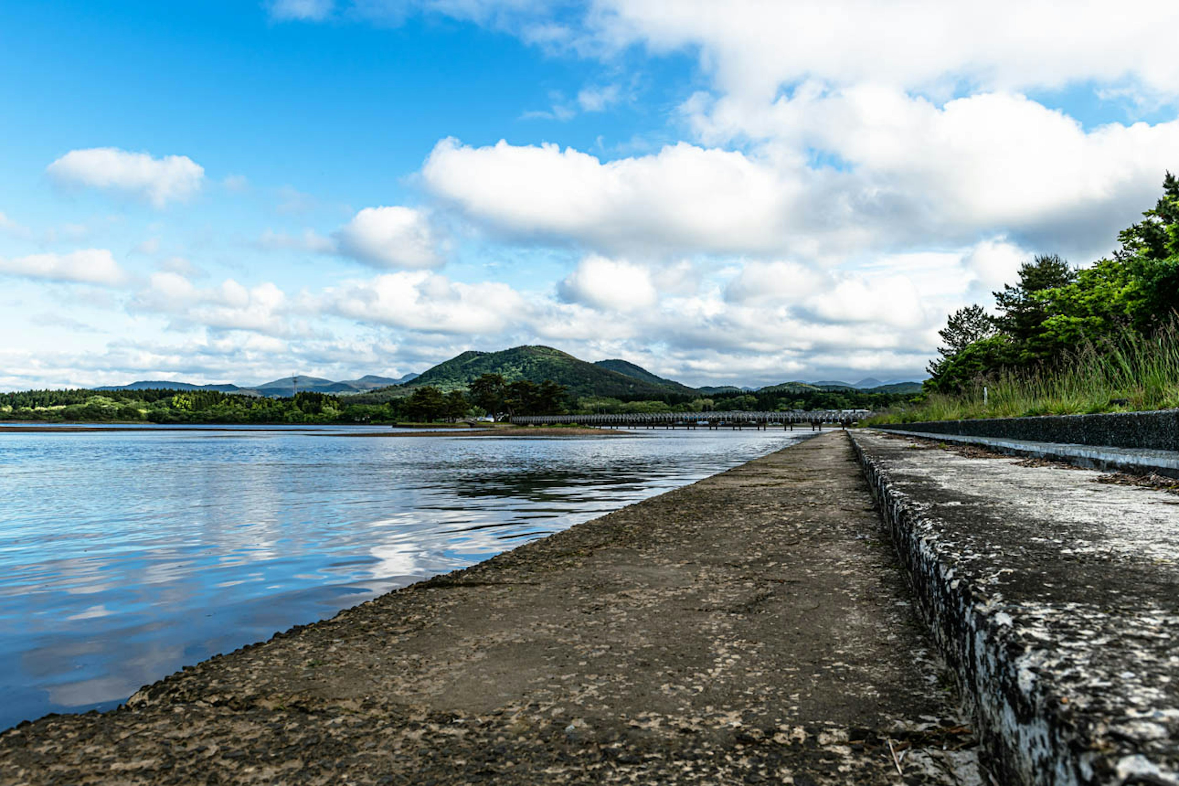 青い空と雲が広がる川の風景 岩の堤防と緑の木々が見える