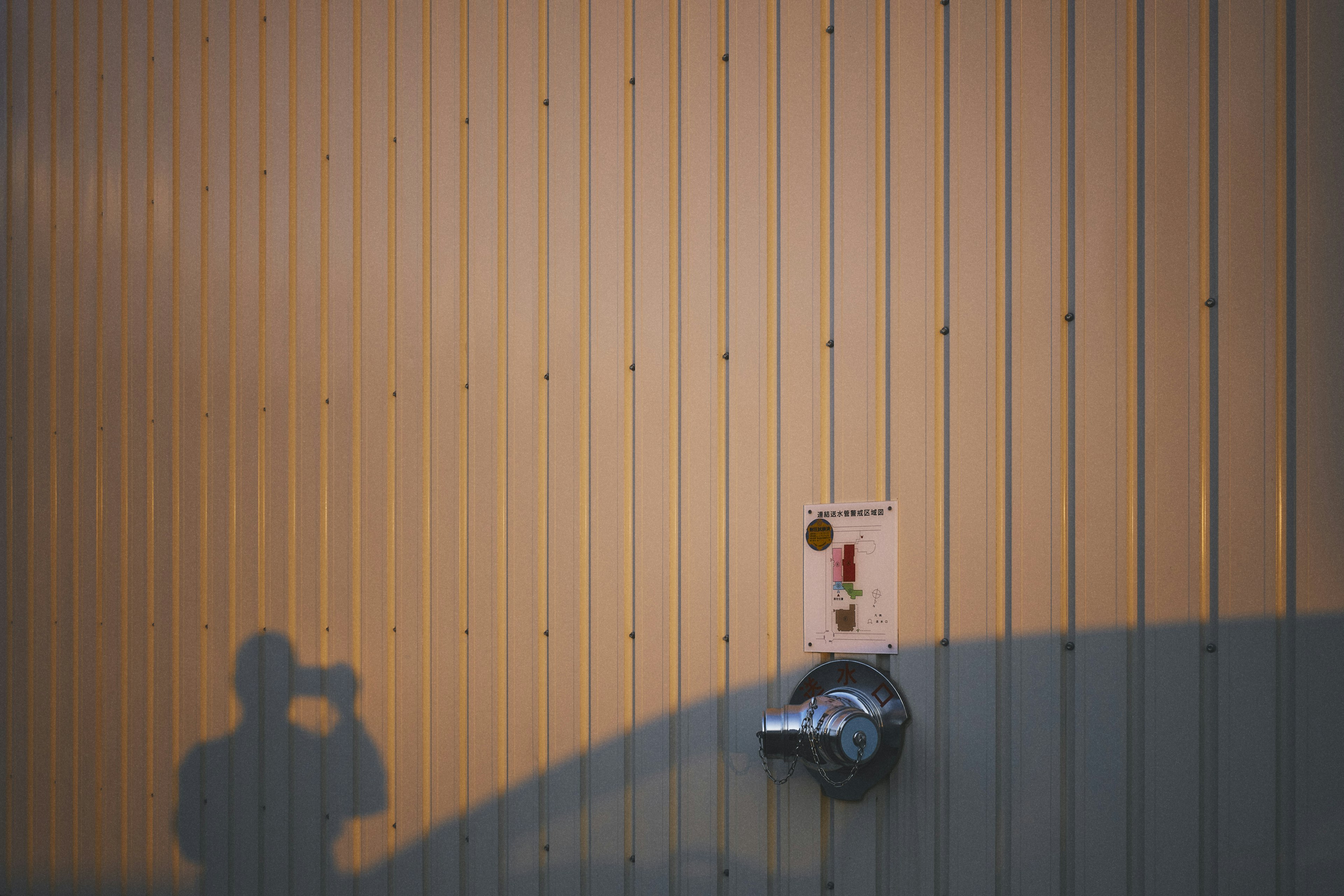 Foto di un muro metallico con un'ombra e un pulsante rosso accanto a un rubinetto