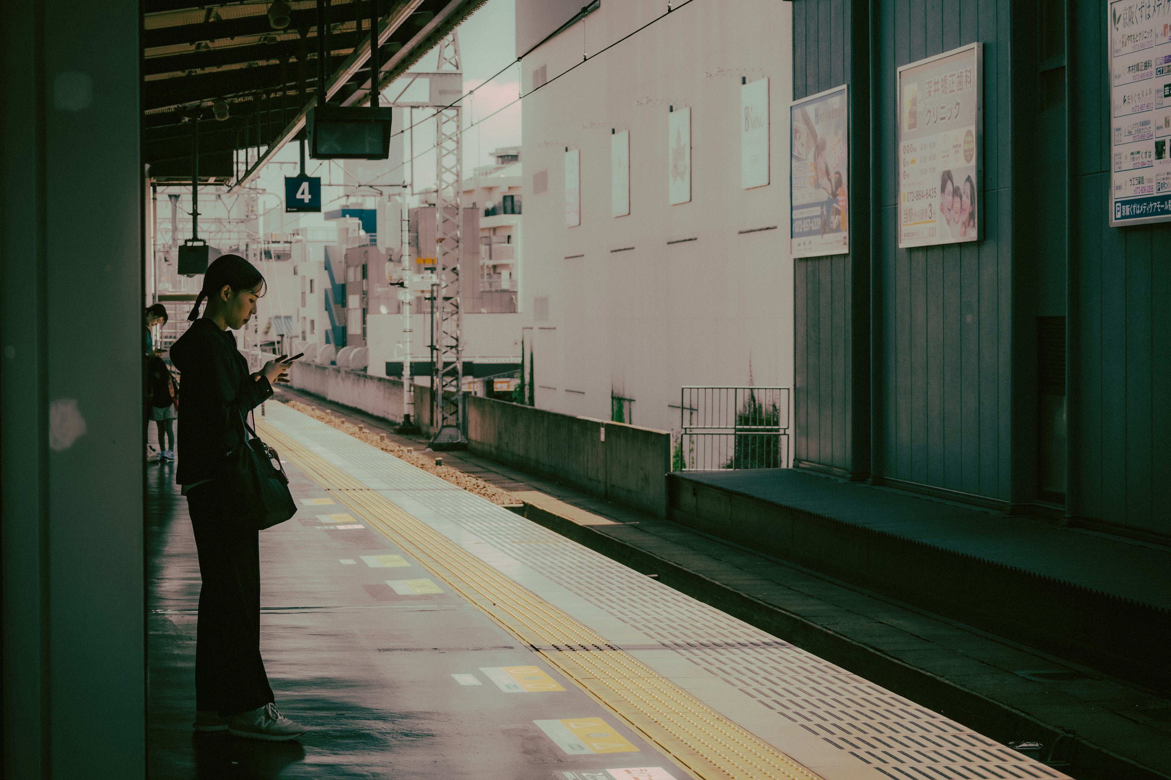 駅のプラットフォームに立つ女性が携帯電話を見ている