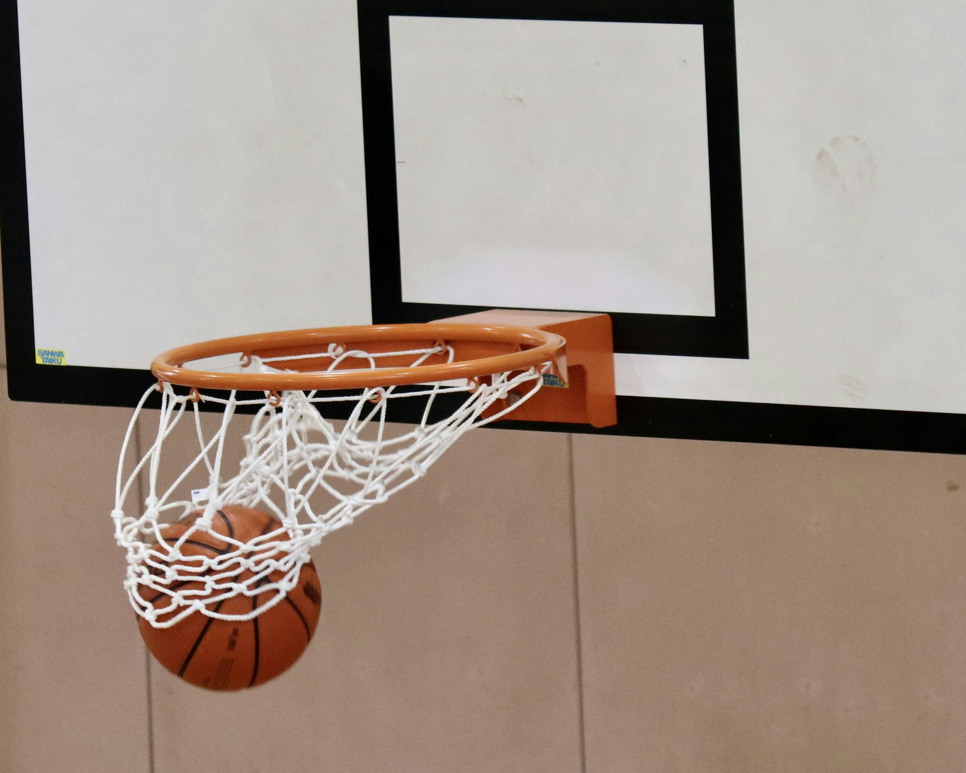 Basketballkorb mit Netz und Ball in einer Turnhalle