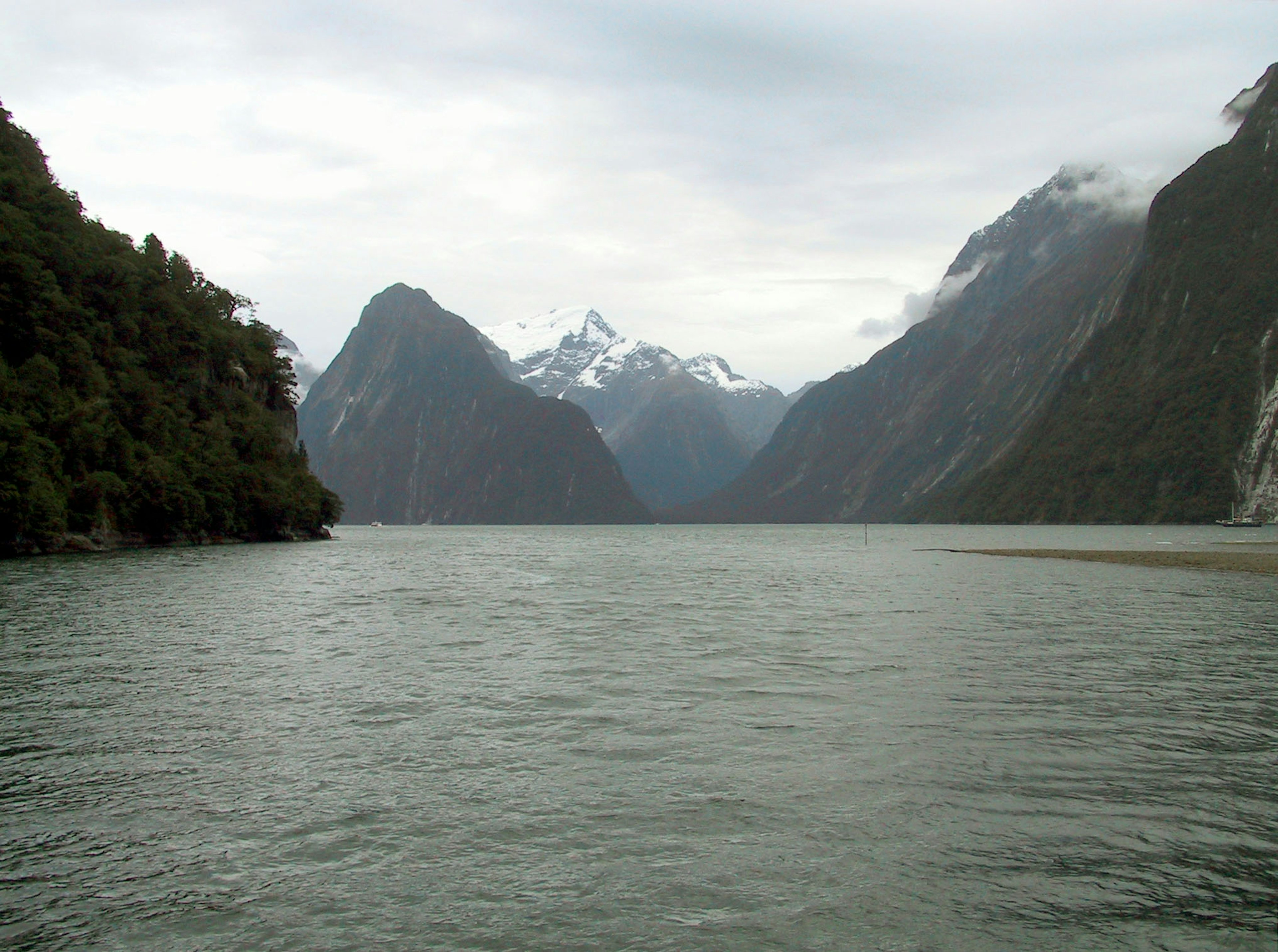 Scenic view of calm water surrounded by majestic mountains with cloudy skies and snow-capped peaks