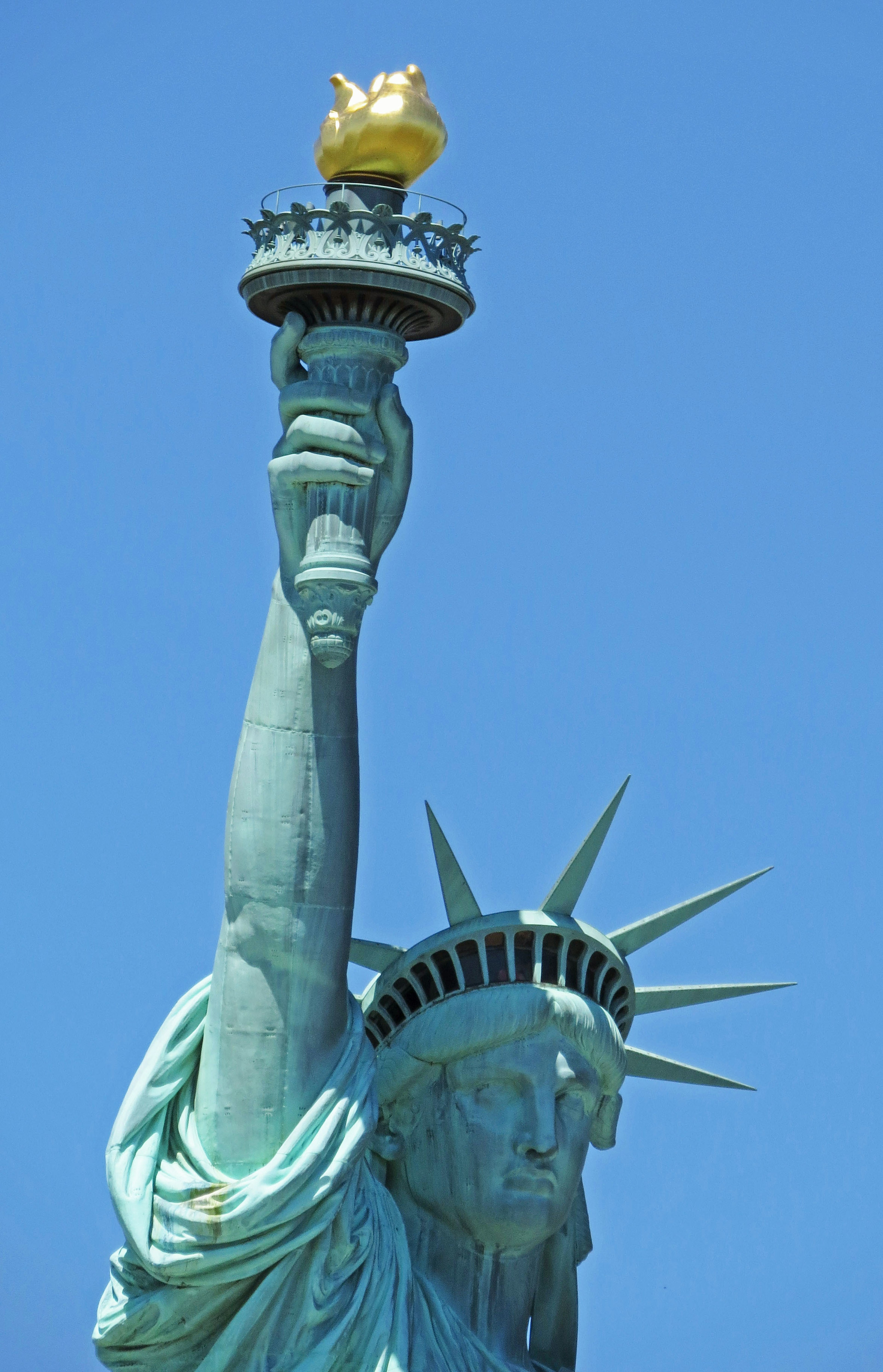 Acercamiento de la Estatua de la Libertad sosteniendo una antorcha bajo un cielo azul