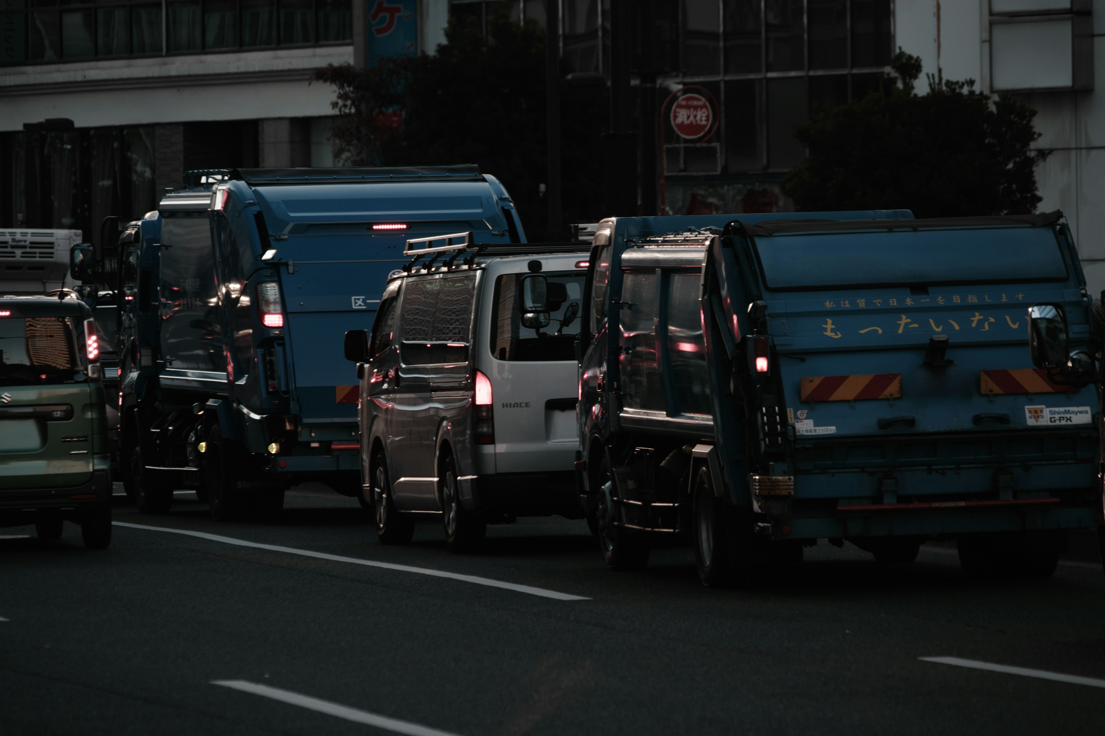 Barisan truk biru dan van putih berhenti di jalan gelap