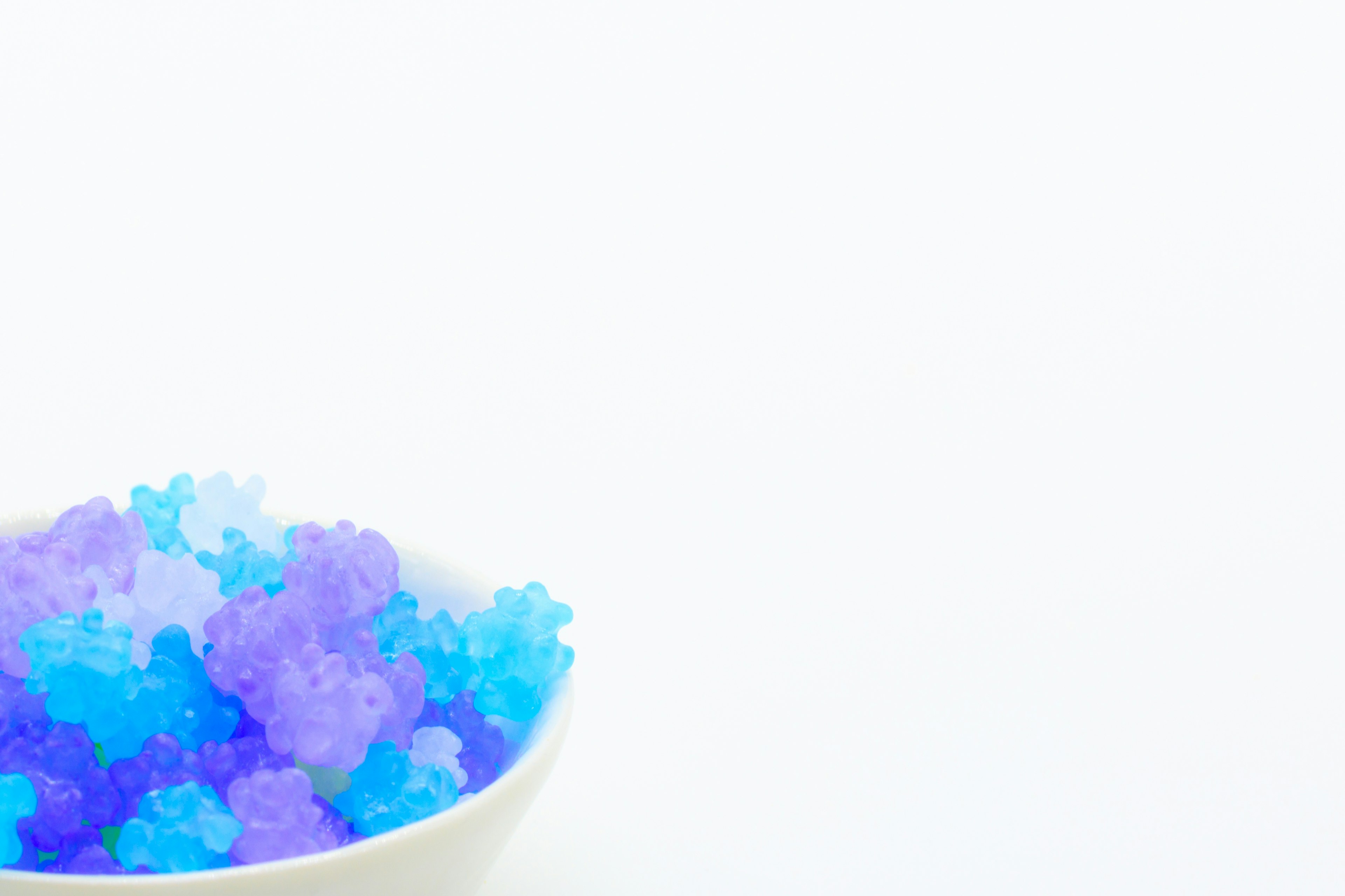 A bowl filled with blue and purple bear-shaped jelly on a white background