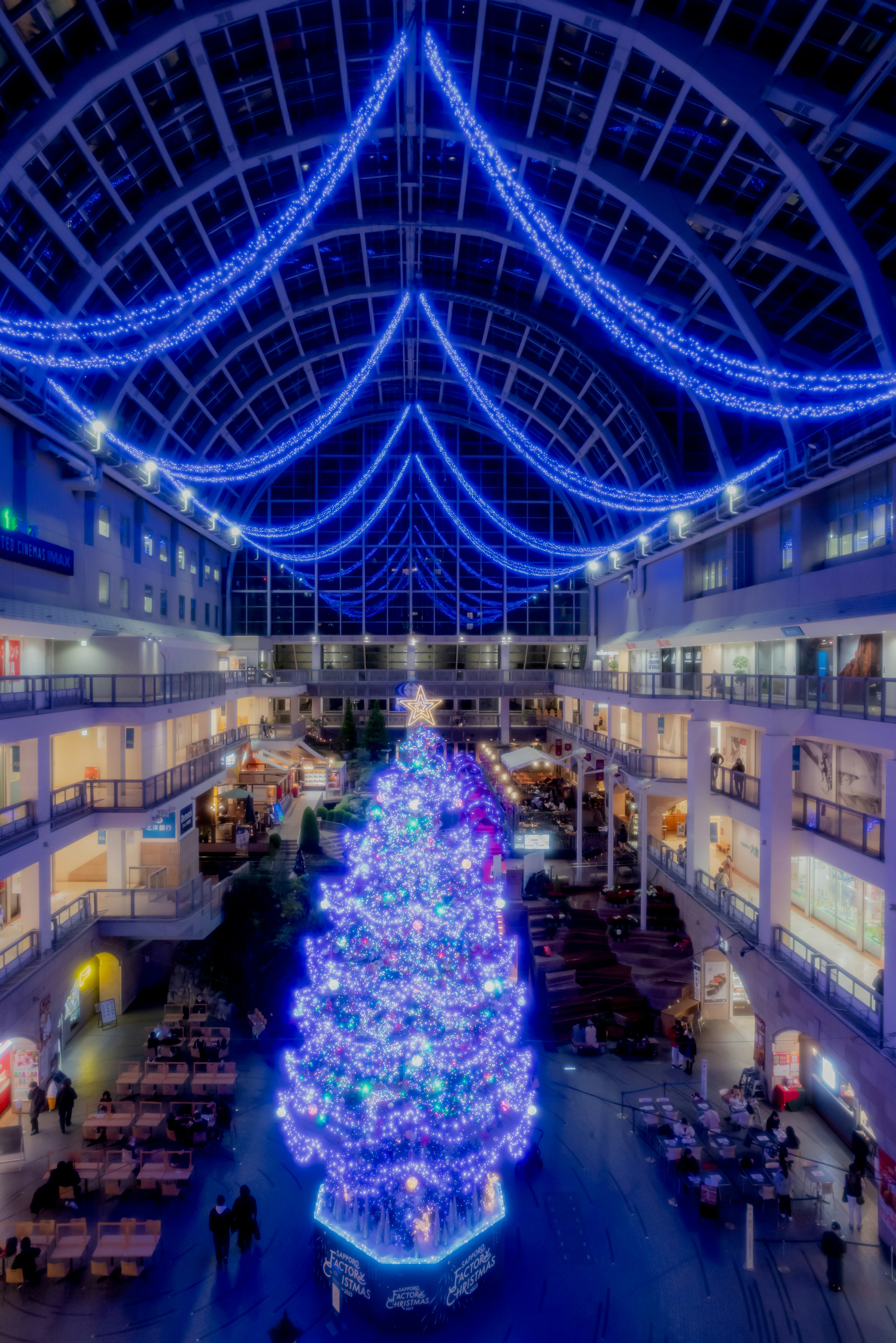 大きなクリスマスツリーが青いイルミネーションで飾られたショッピングモールの内部