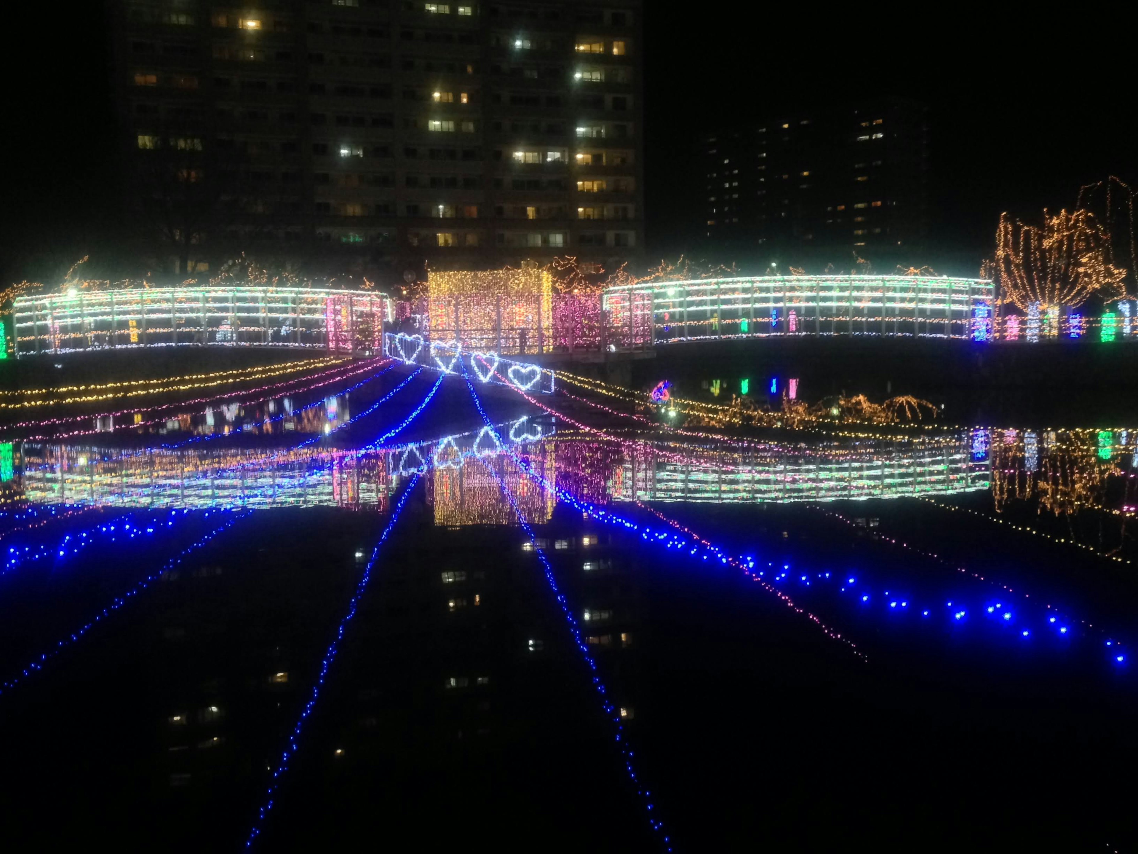 Beleuchtete Brücke mit bunten Lichtern, die sich nachts auf dem Wasser spiegeln