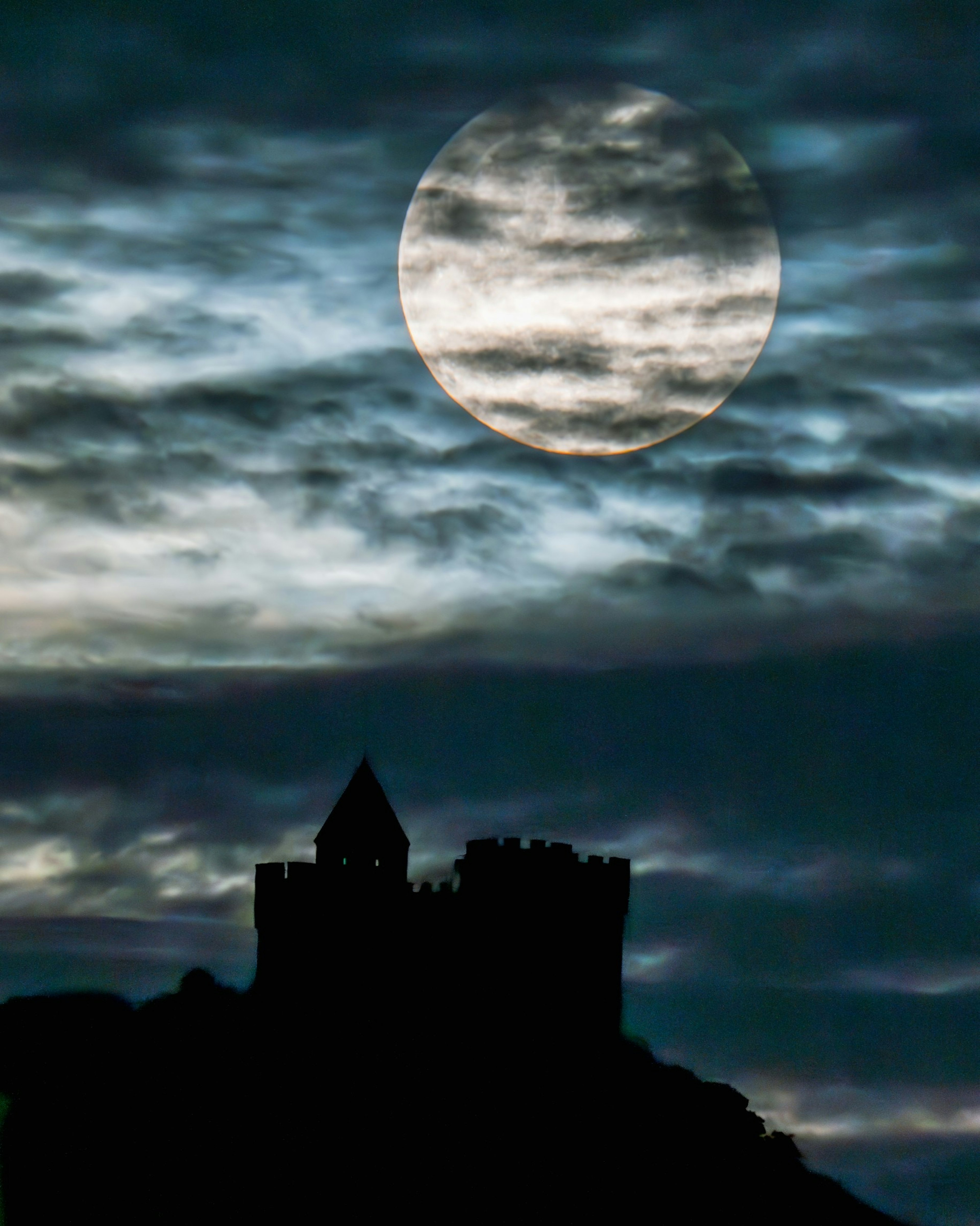 Silhouette of a castle against a cloudy sky with a large moon