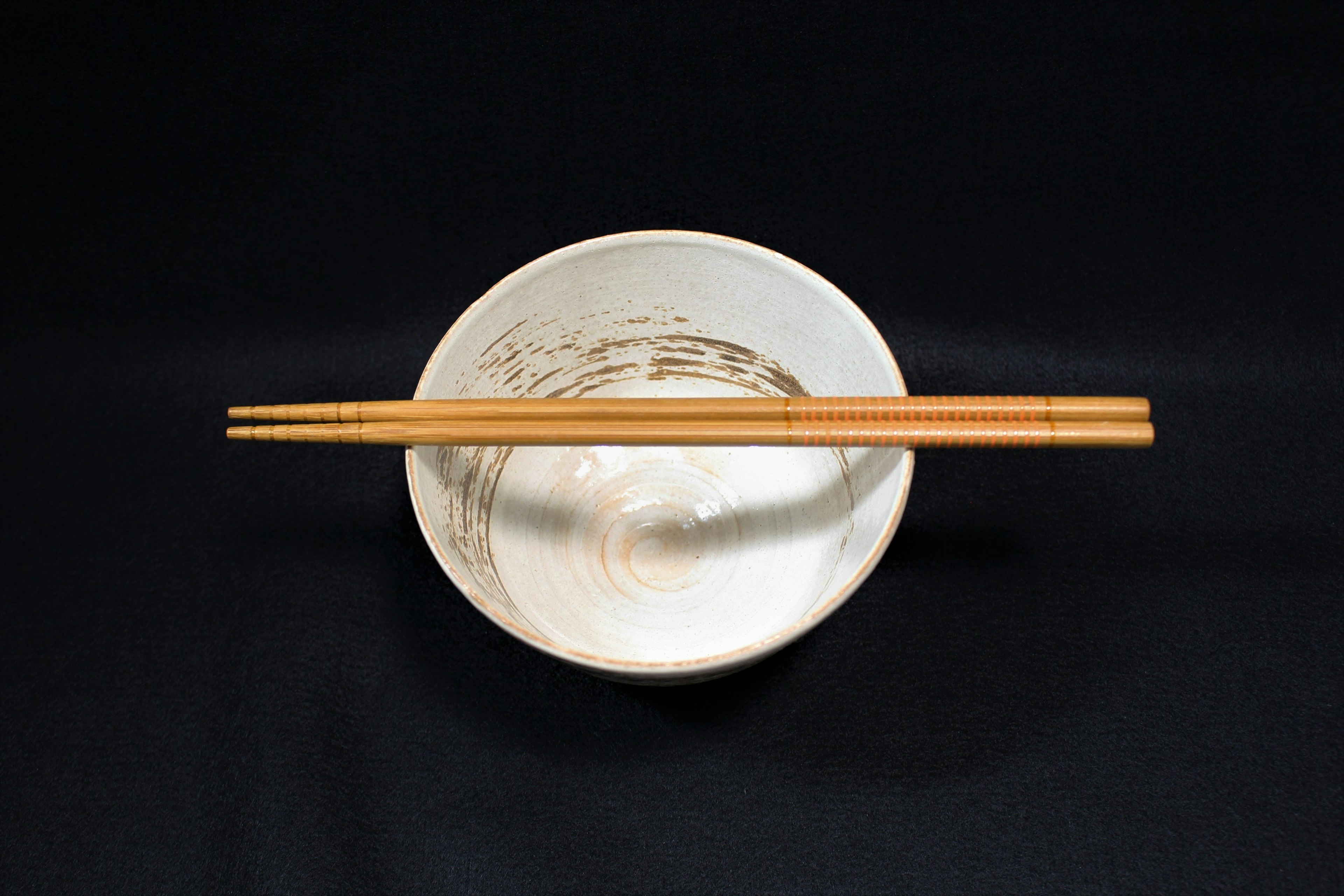 Wooden chopsticks resting on a white bowl against a black background