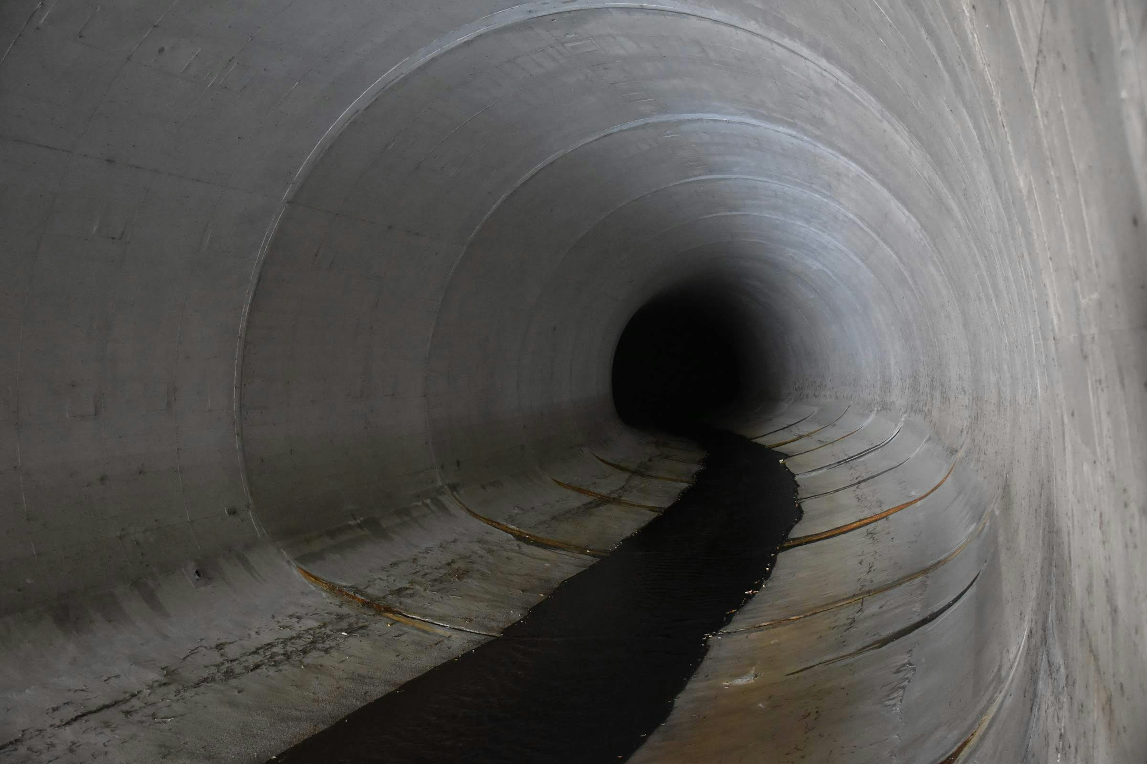 Vista interna di un tunnel in cemento con flusso d'acqua scura