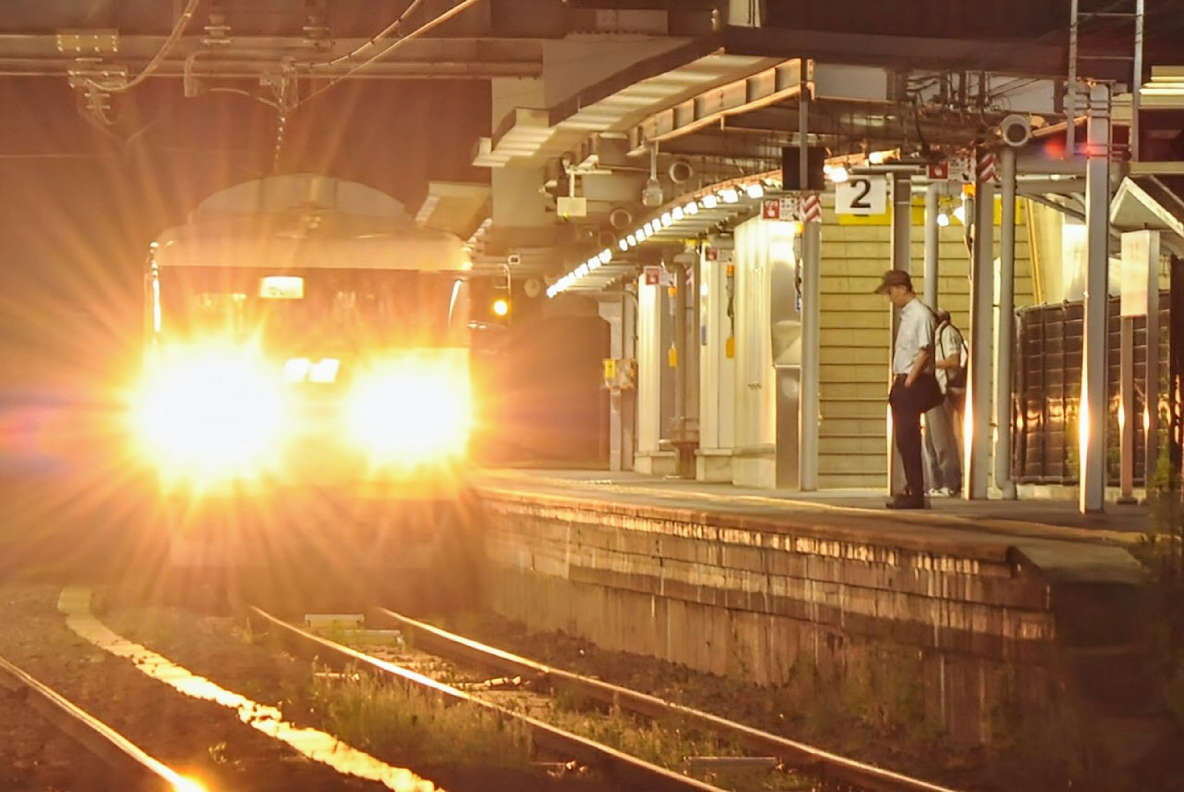 Train approaching a station at night with a waiting passenger