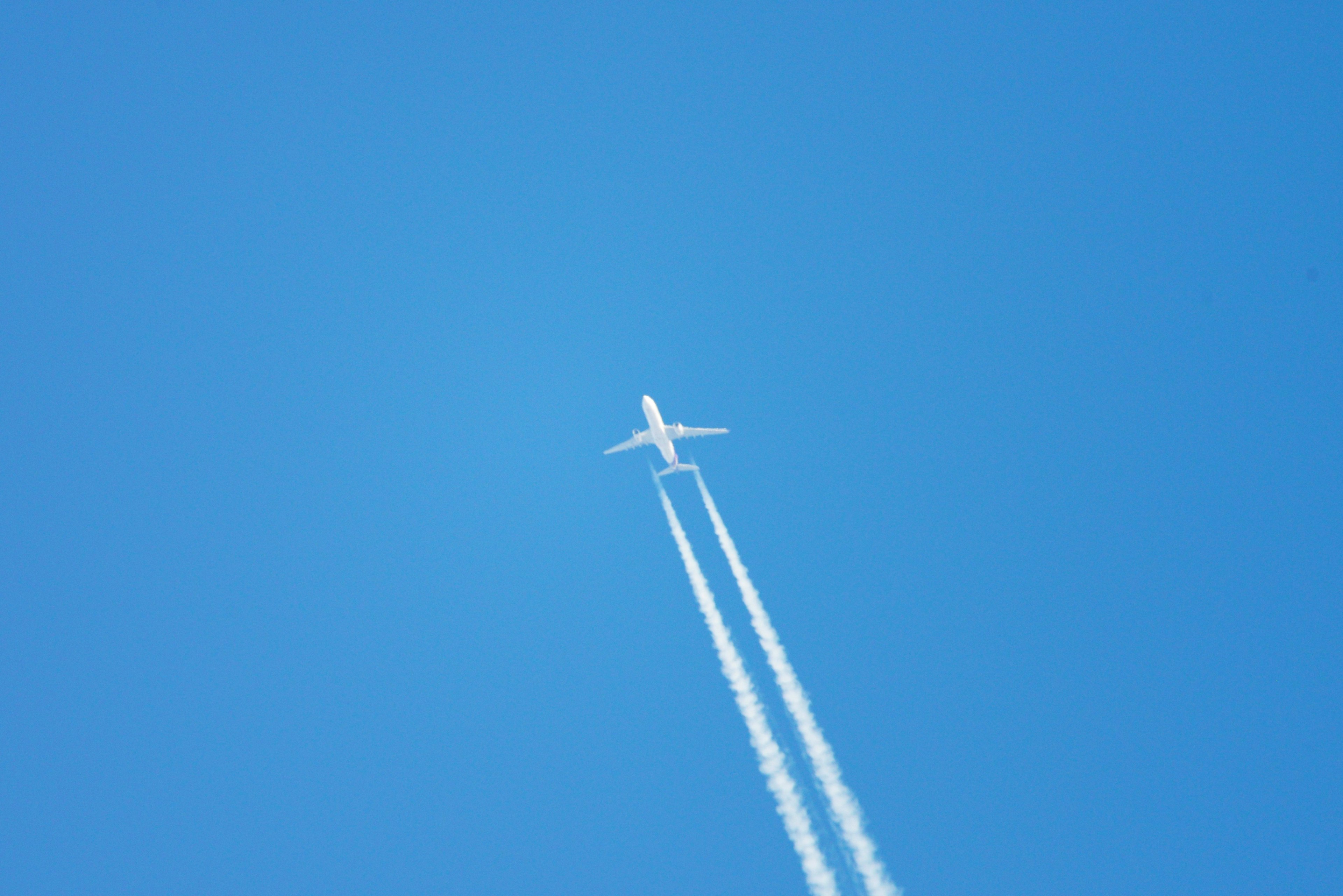 Un aereo che vola in un cielo blu chiaro lasciando scie bianche