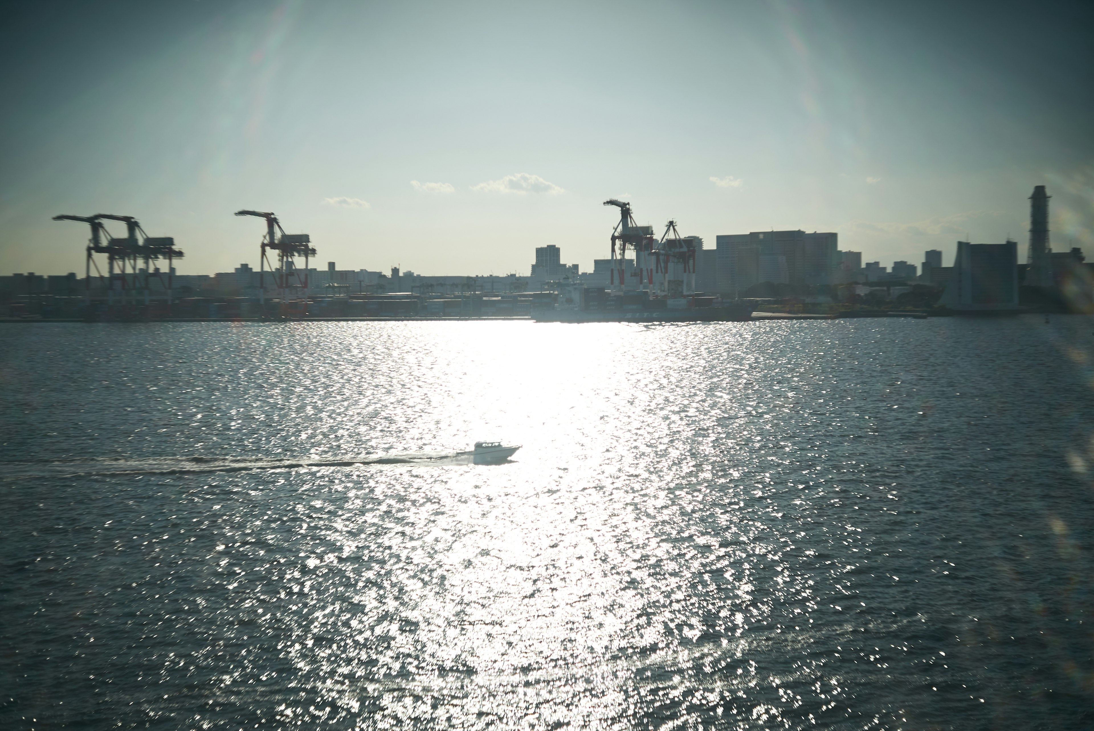 A small boat gliding on the shimmering water with distant cranes visible