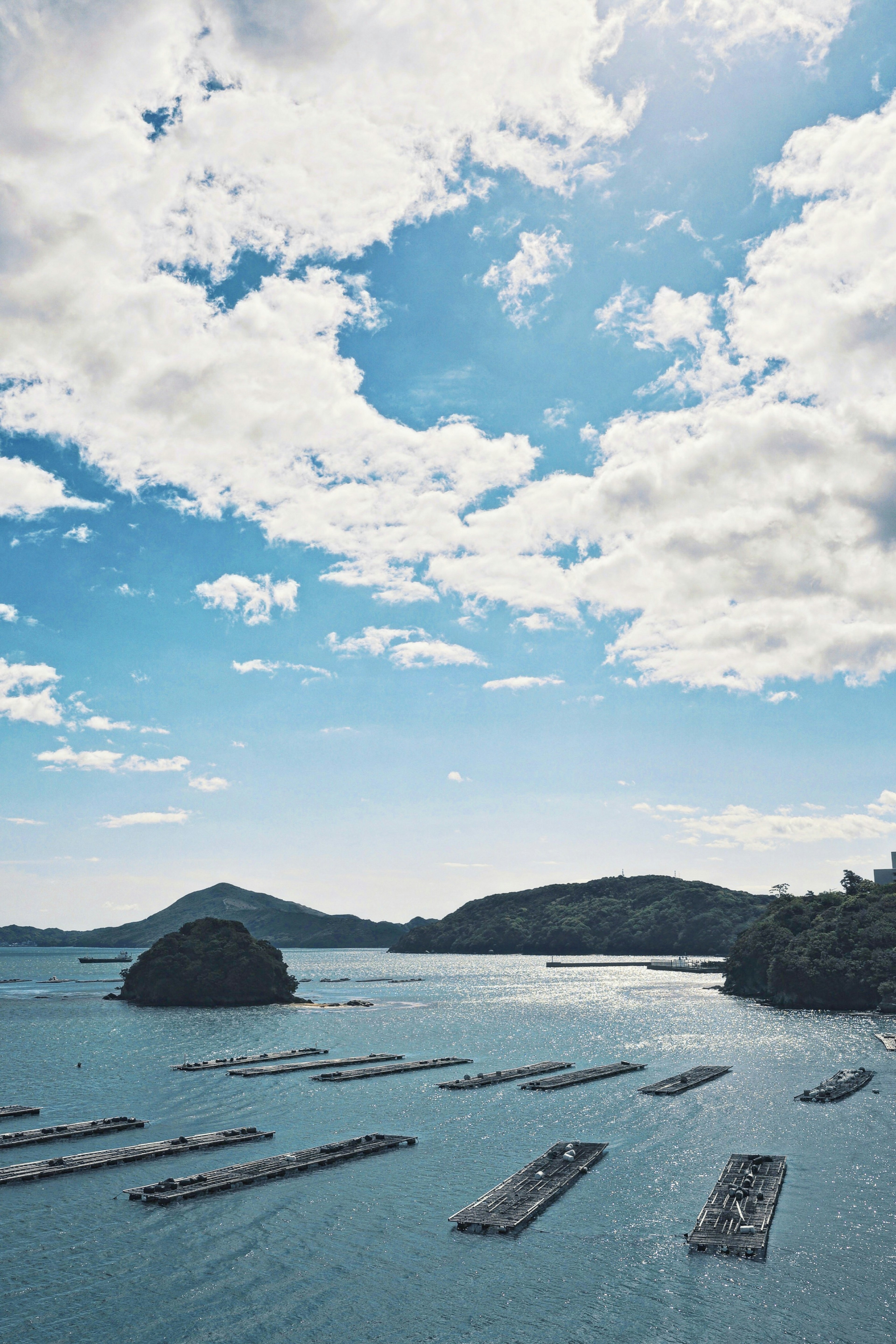 Vista panoramica di zattere di acquacoltura galleggianti in acqua blu sotto un cielo parzialmente nuvoloso